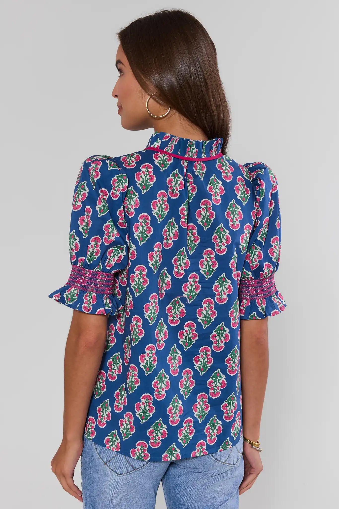 Woman standing wearing a blue floral blouse against a plain background