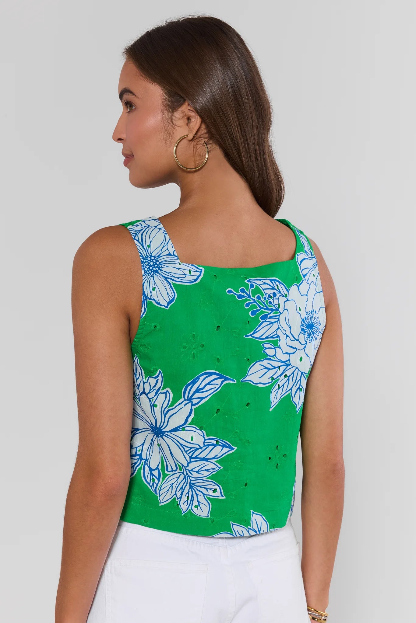 Woman standing wearing a green sleeveless top with blue floral patterns on a plain background