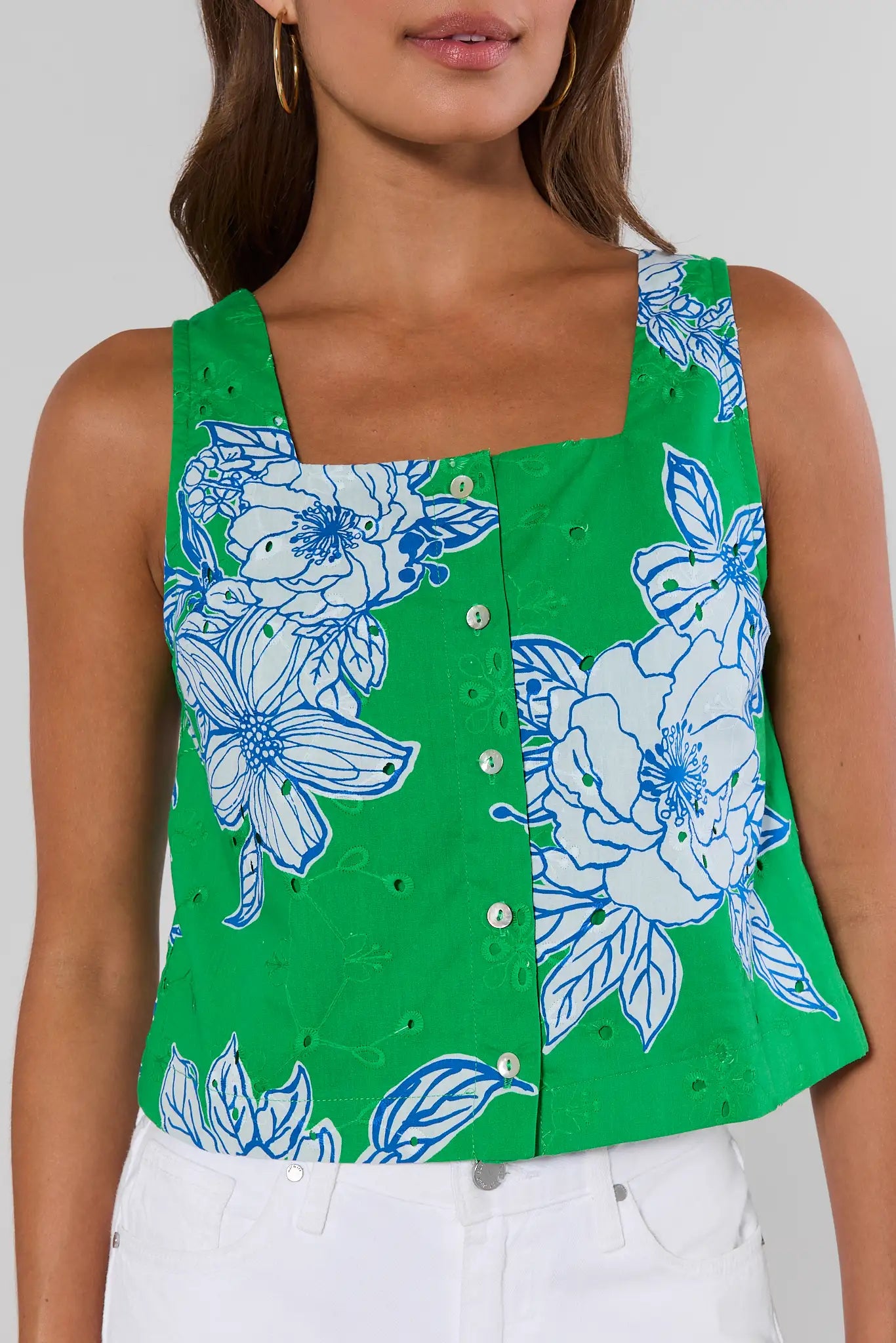 Green sleeveless top with blue floral pattern worn by a person on a plain background close up