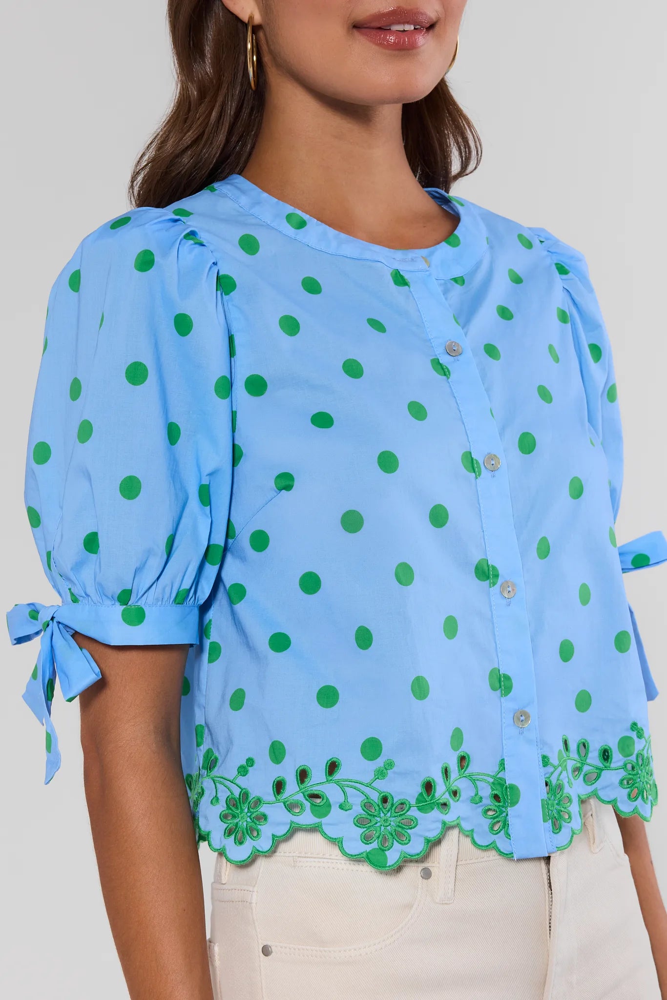 Woman wearing a blue blouse with green polka dots and lace details on a plain background close up