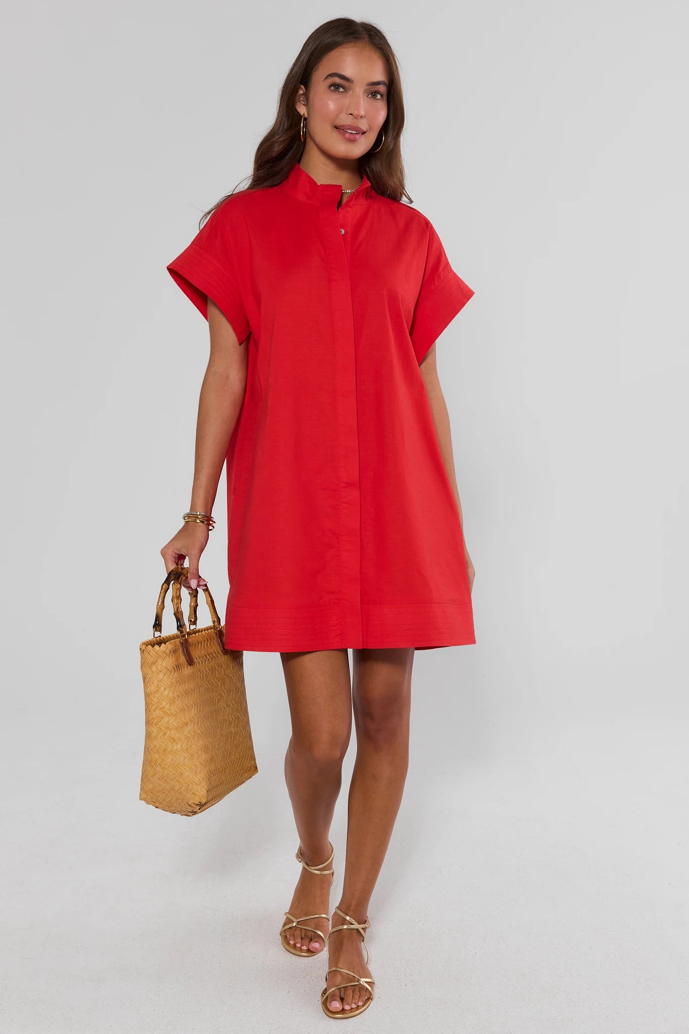 Woman wearing a red dress holding a straw bag on a white background