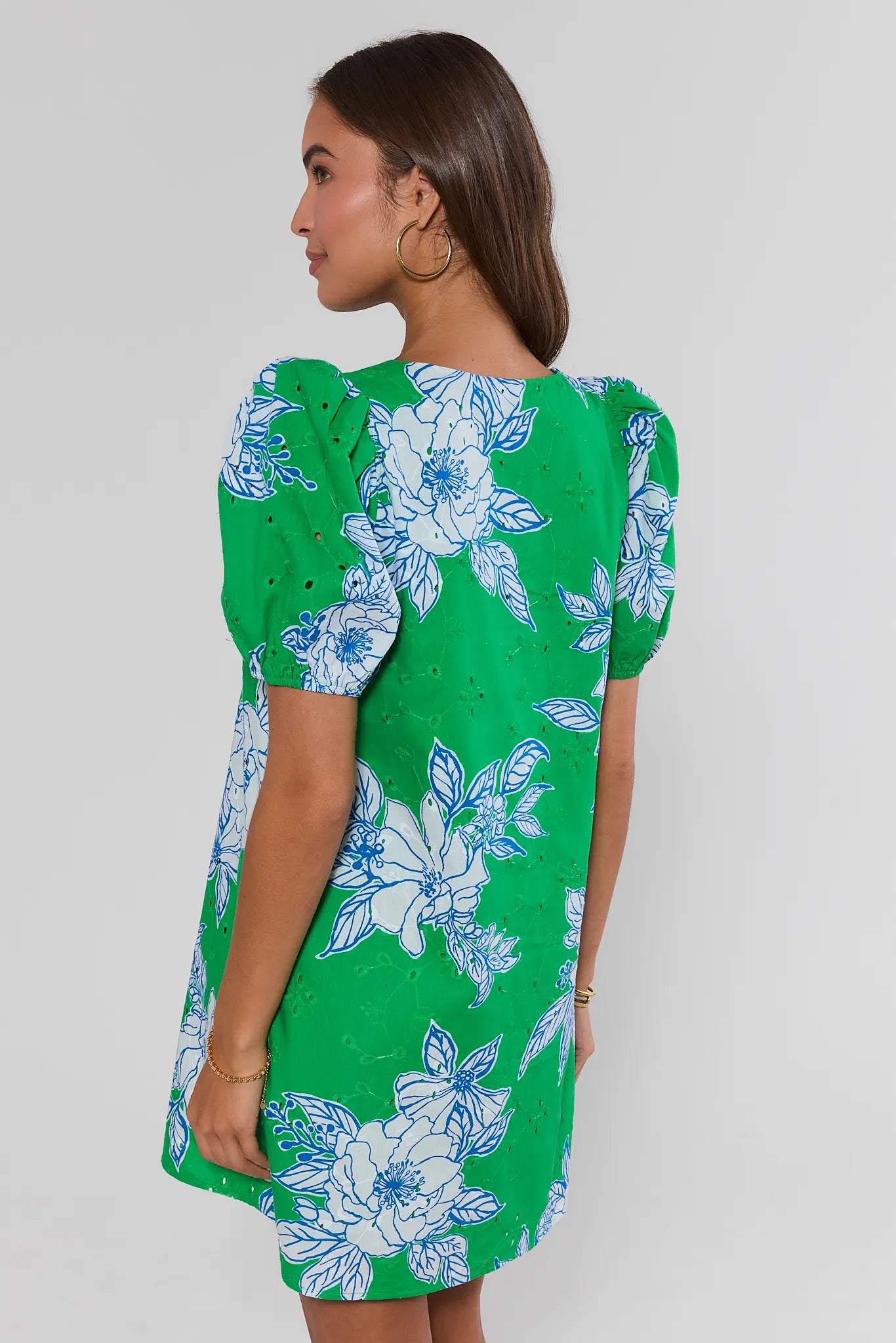 Woman standing wearing a green dress with blue floral pattern on a plain background