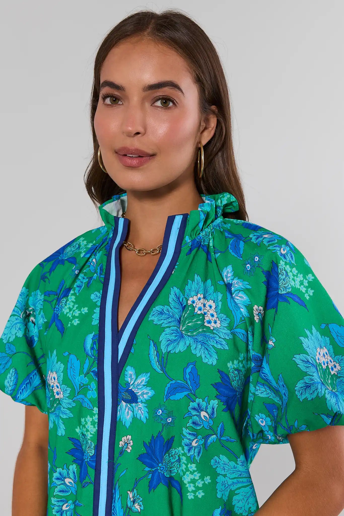 Woman wearing a green floral patterned top with a white background close up