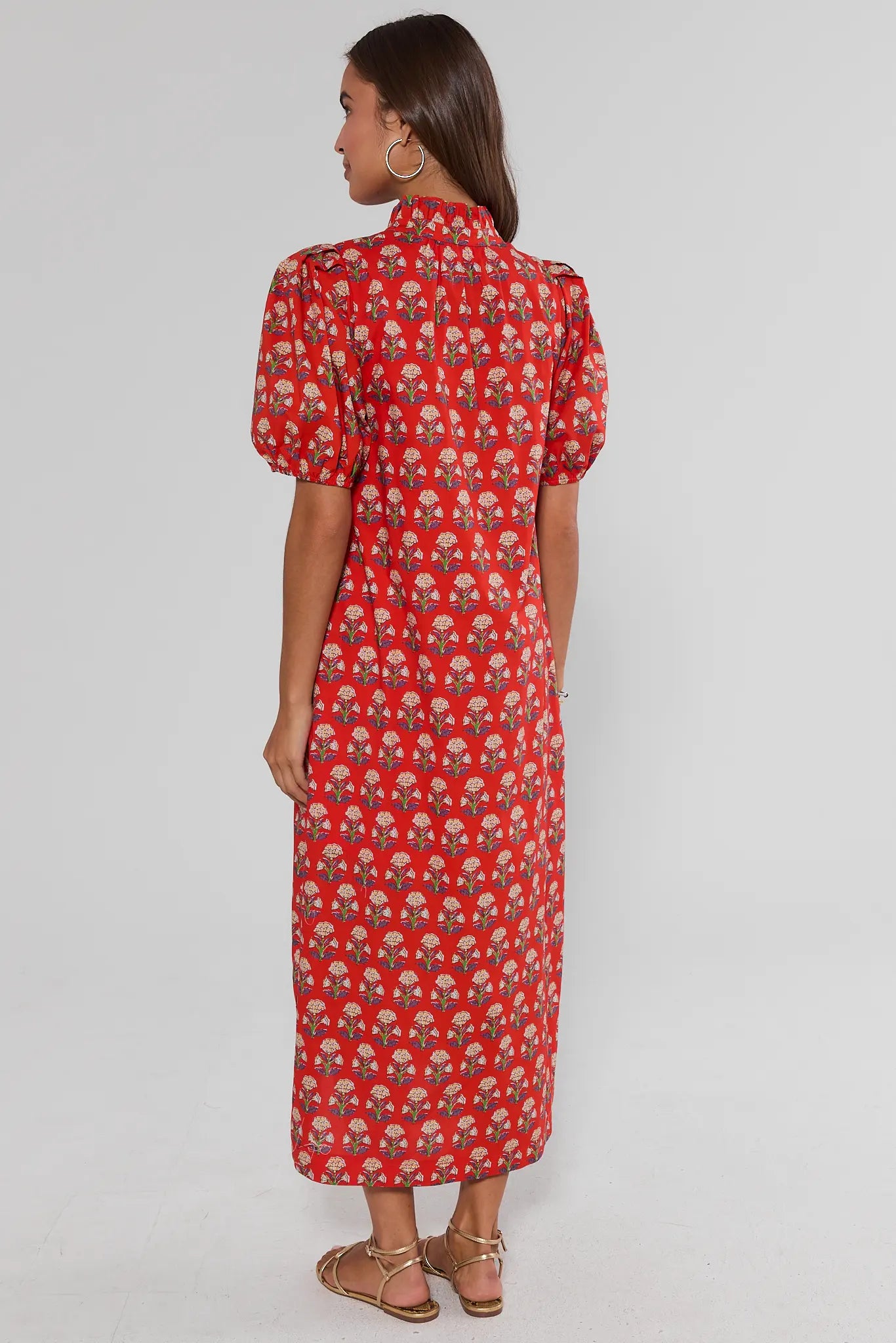 Woman wearing a red patterned dress on a gray background walking