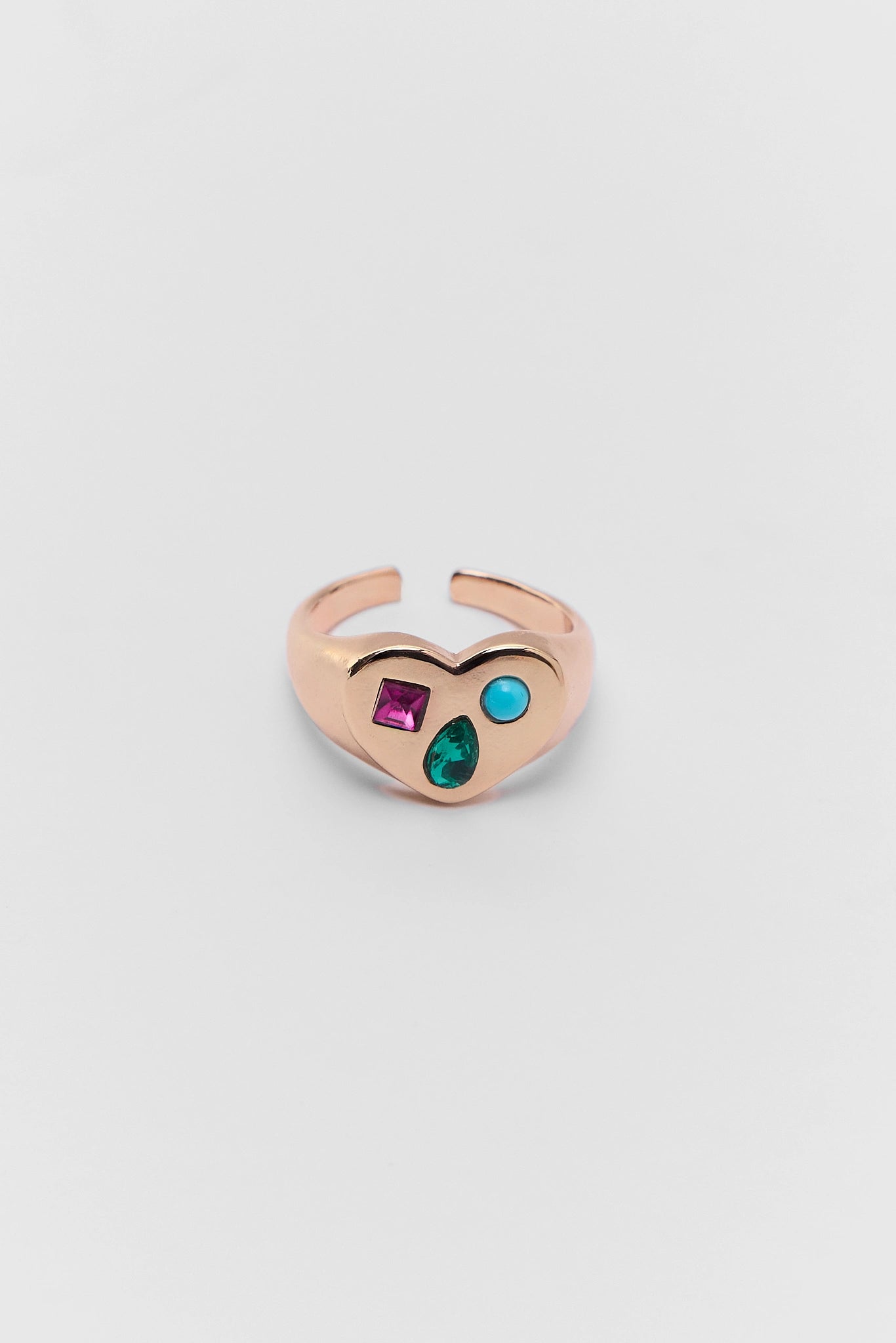 Rose gold heart-shaped ring with gemstones on a light gray background
