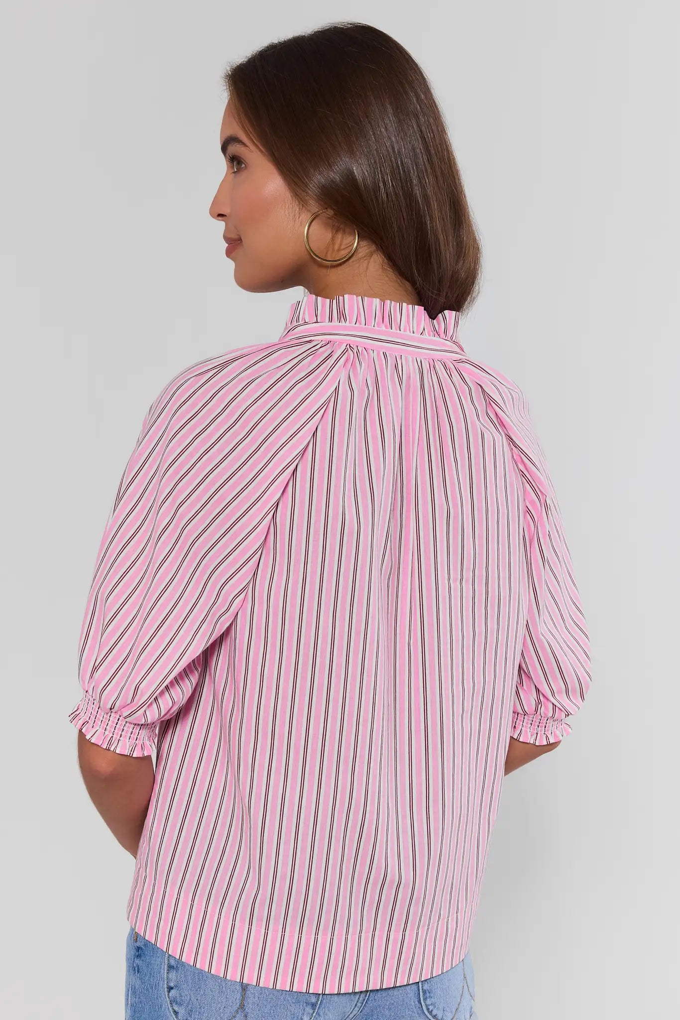 Woman wearing a pink and white striped blouse against a plain background standing