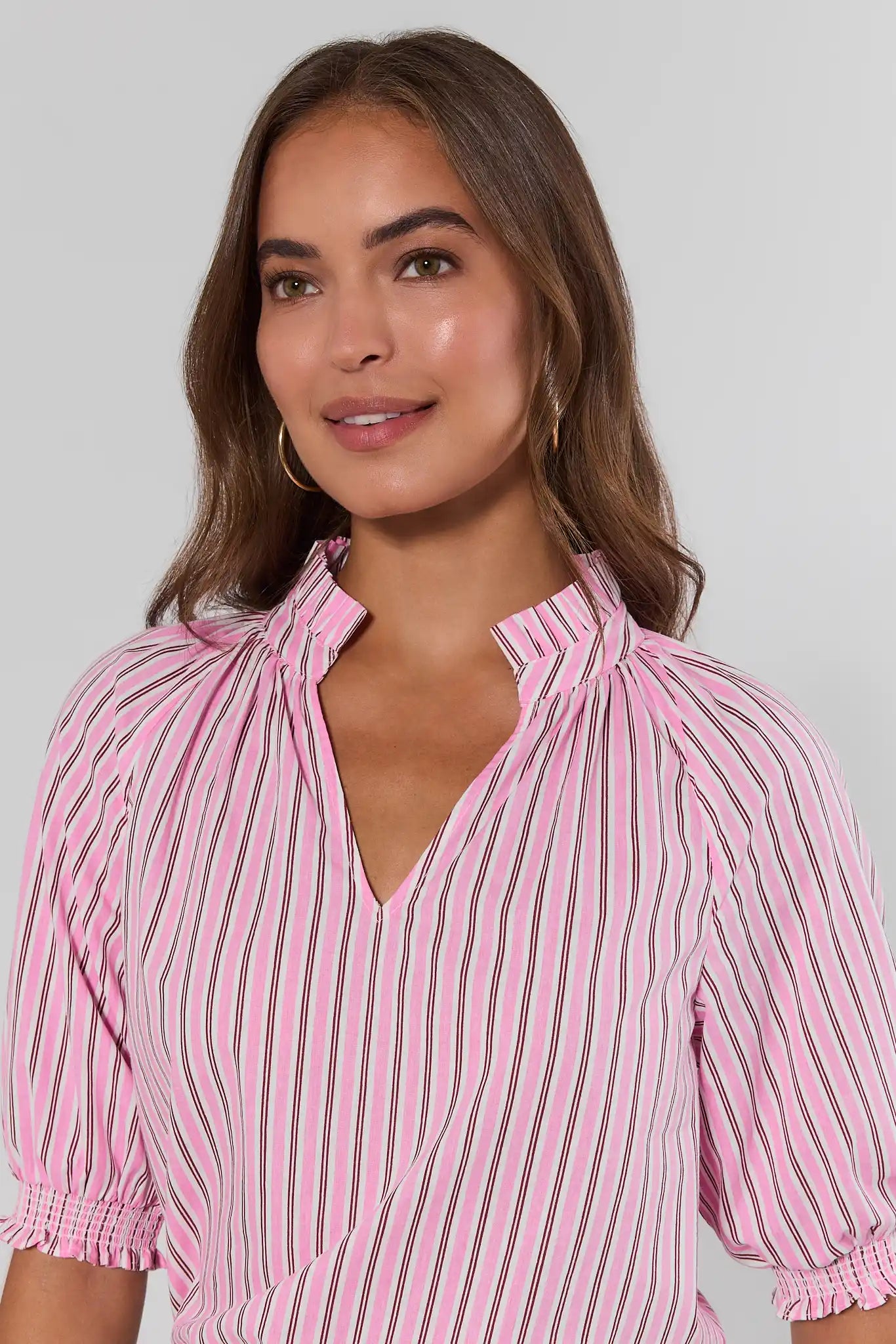 Woman wearing a pink and white striped blouse against a plain background close up