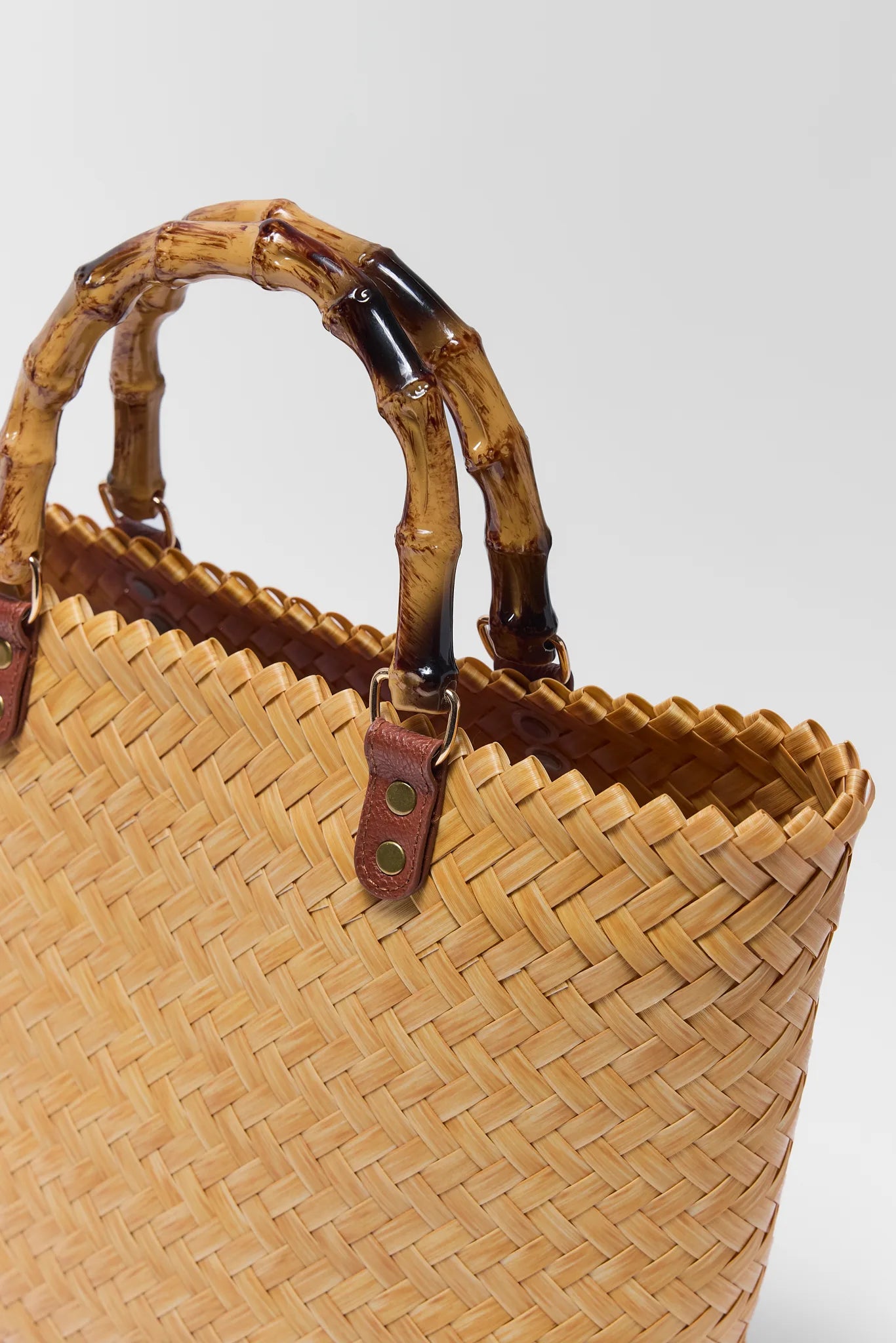Woven straw bag with bamboo handles on a white background close up