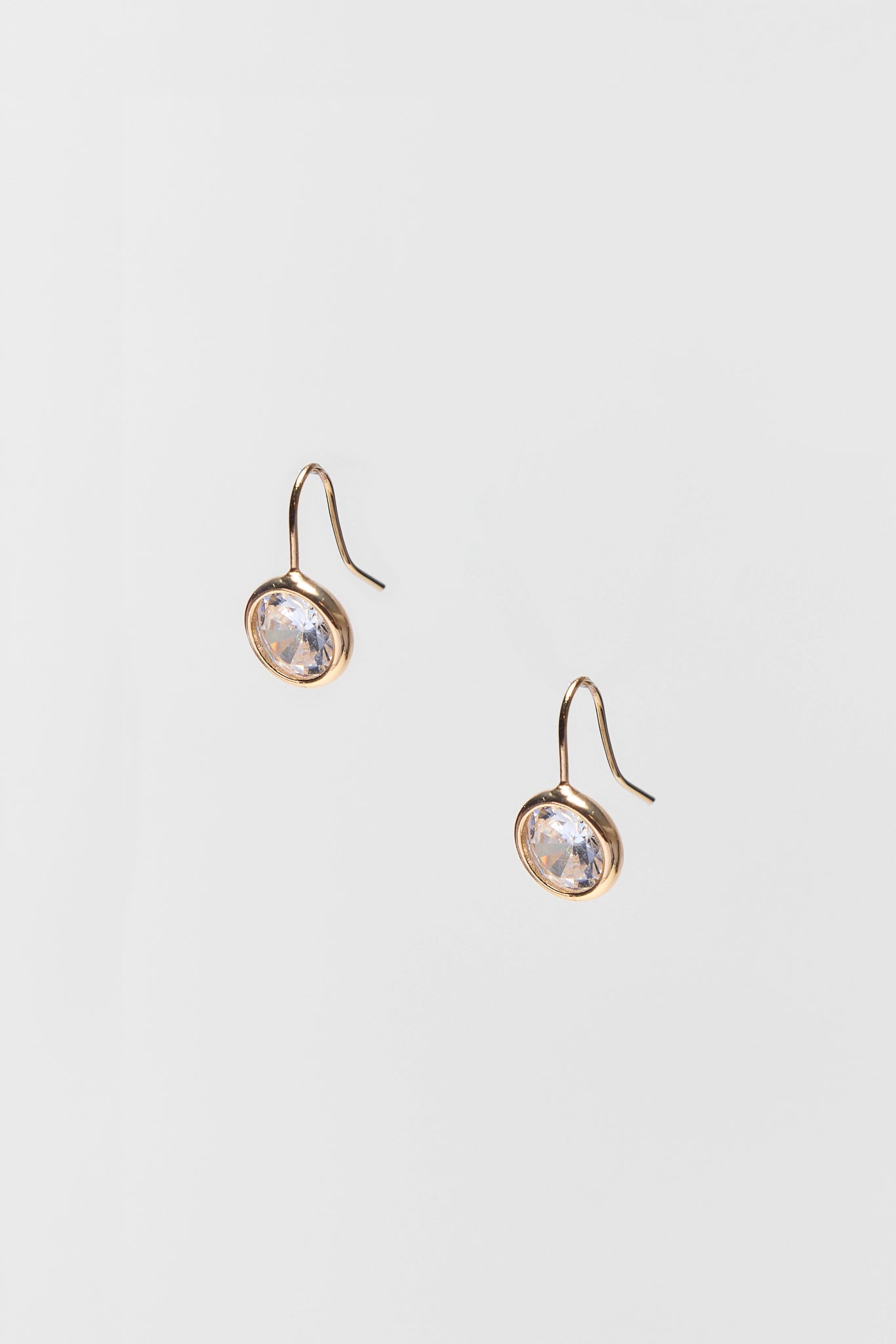 Pair of gold earrings with clear gemstones on a light gray background