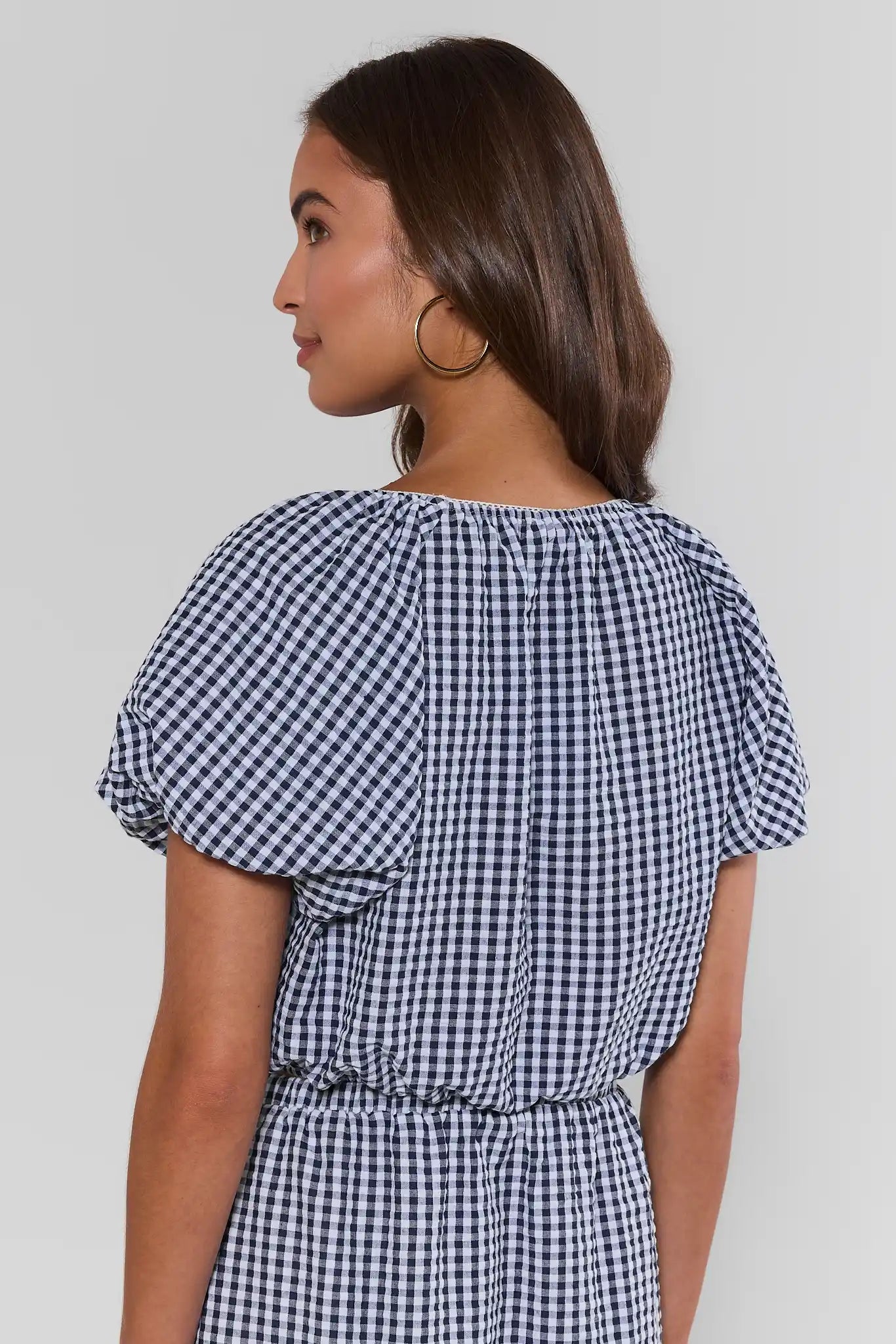 Woman wearing a blue and white checkered top against a plain background standing