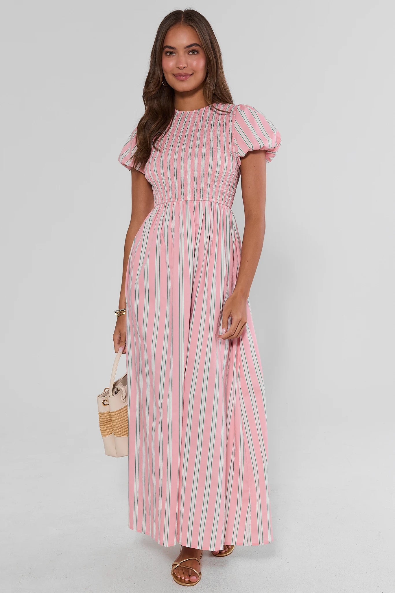 Woman wearing a pink and white striped dress on a plain background standing