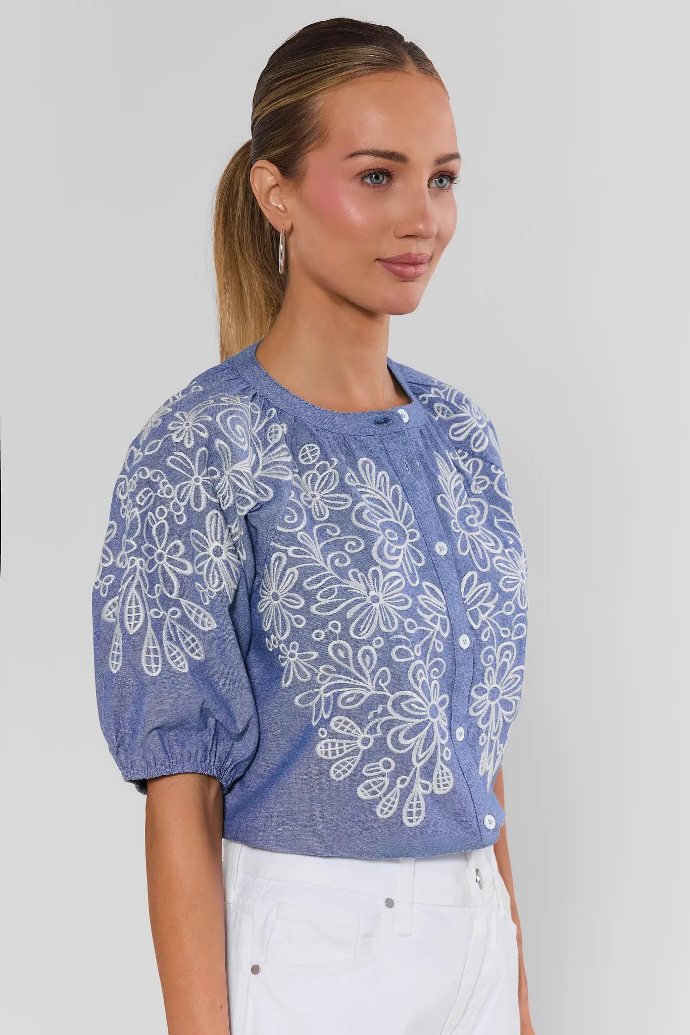 Woman wearing a blue floral patterned blouse against a plain background close up side