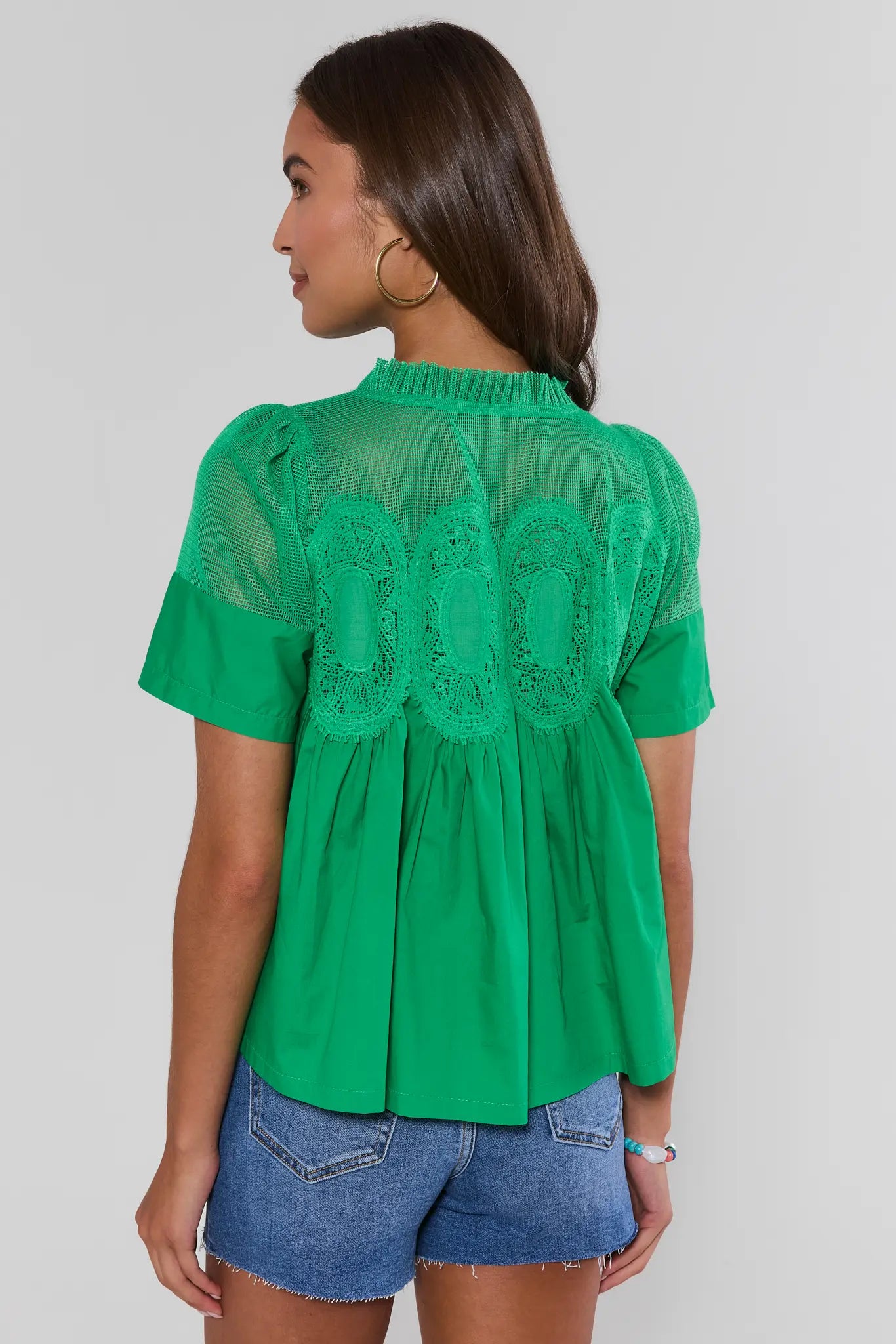 Woman wearing a green blouse with lace details on a plain background standing