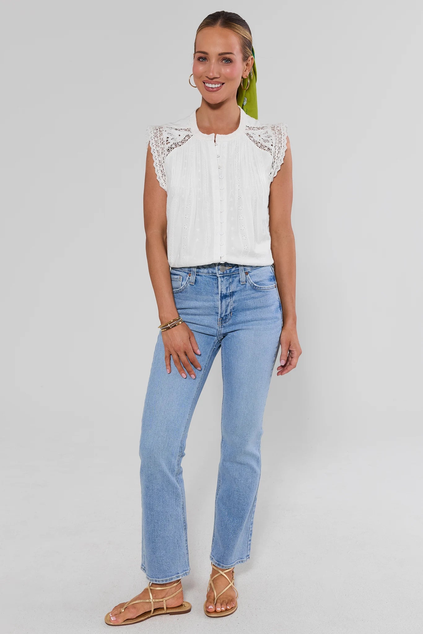 Woman wearing a white lace top and blue jeans on a plain background standing