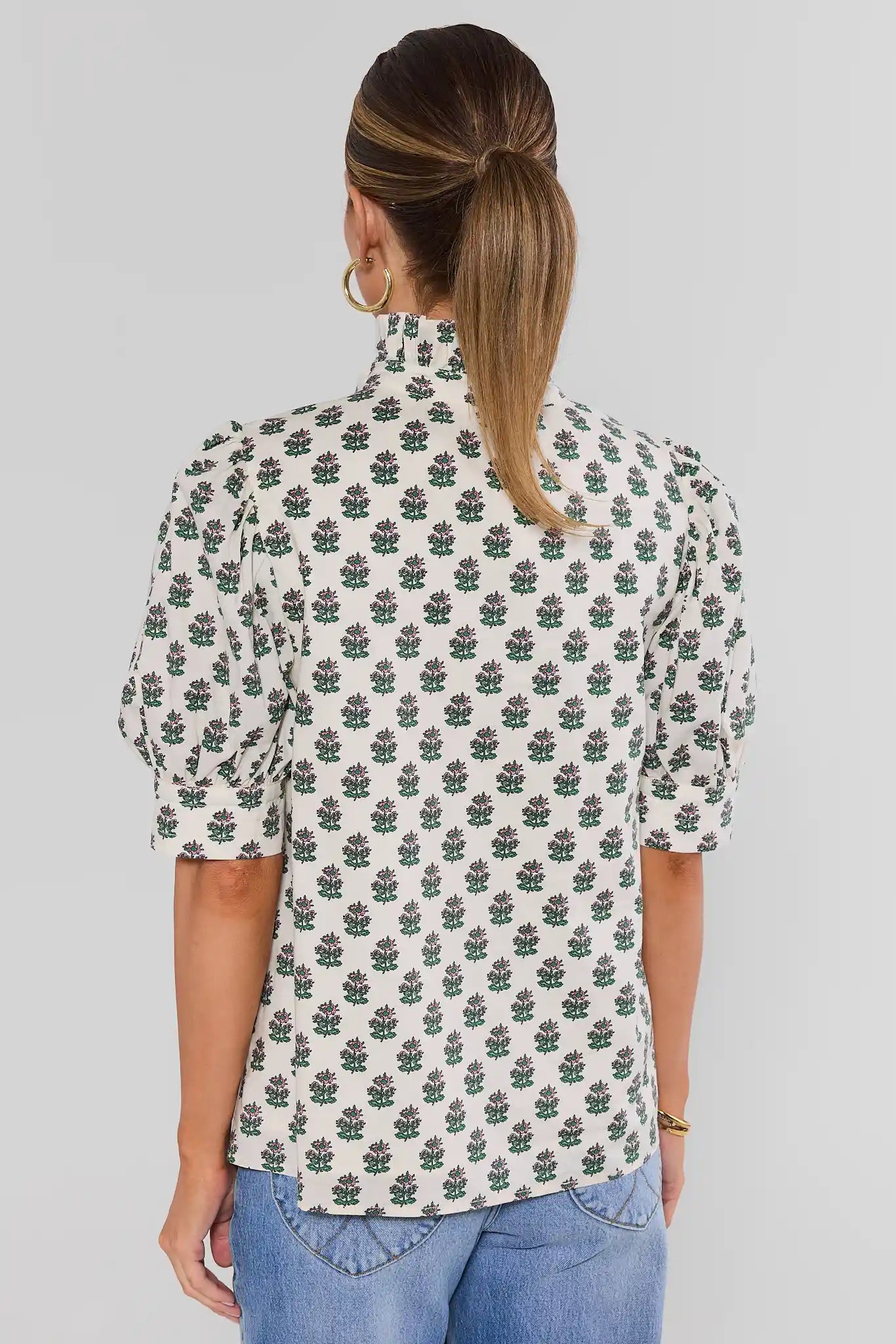 Woman wearing a floral patterned shirt on a plain background stand