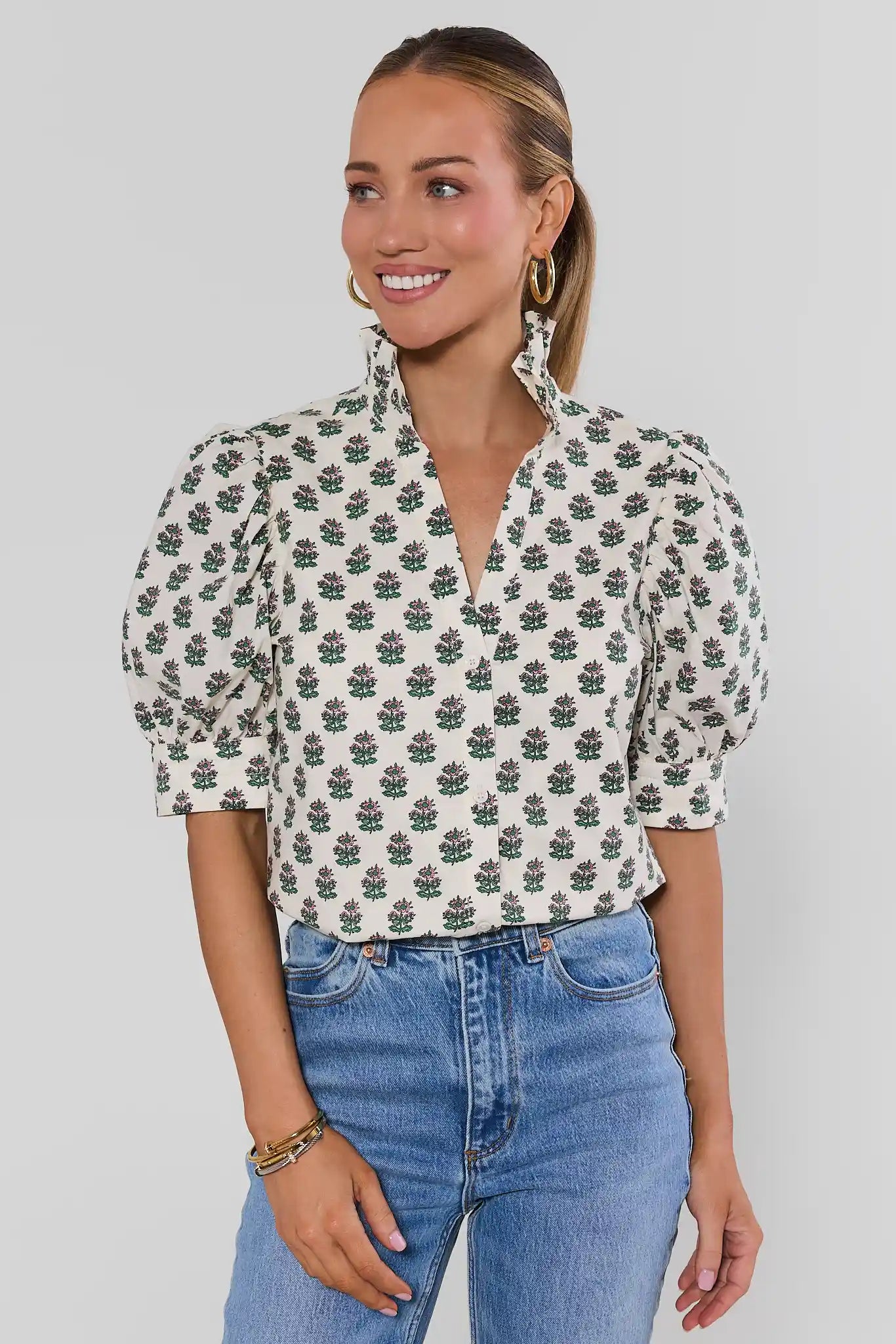 Woman wearing a floral blouse and jeans against a plain background