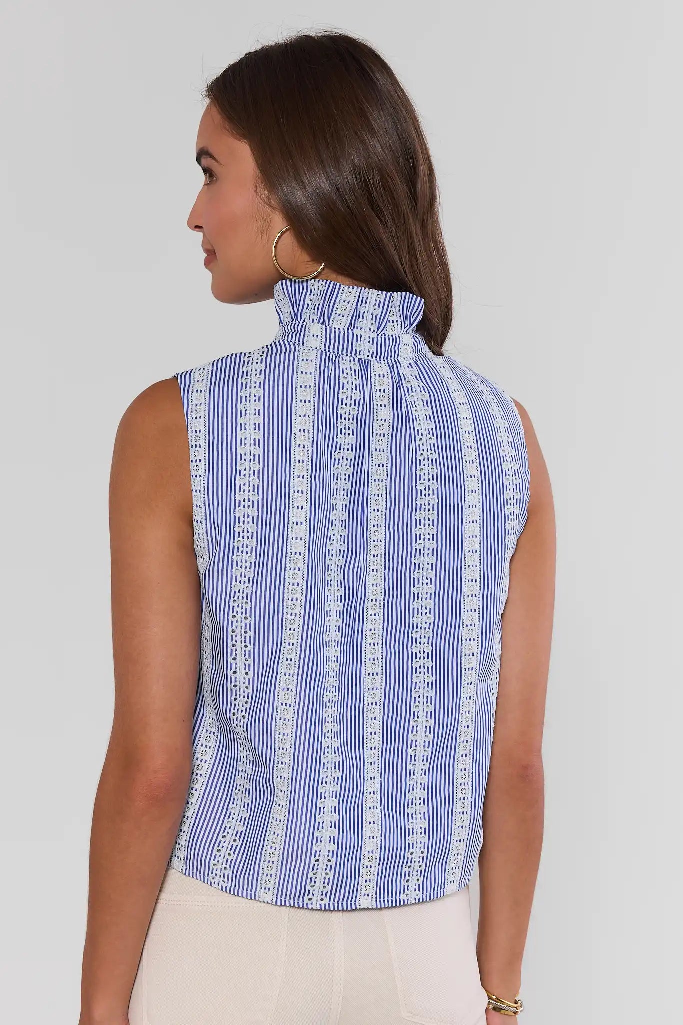 Woman wearing a blue and white patterned sleeveless top against a plain background standing