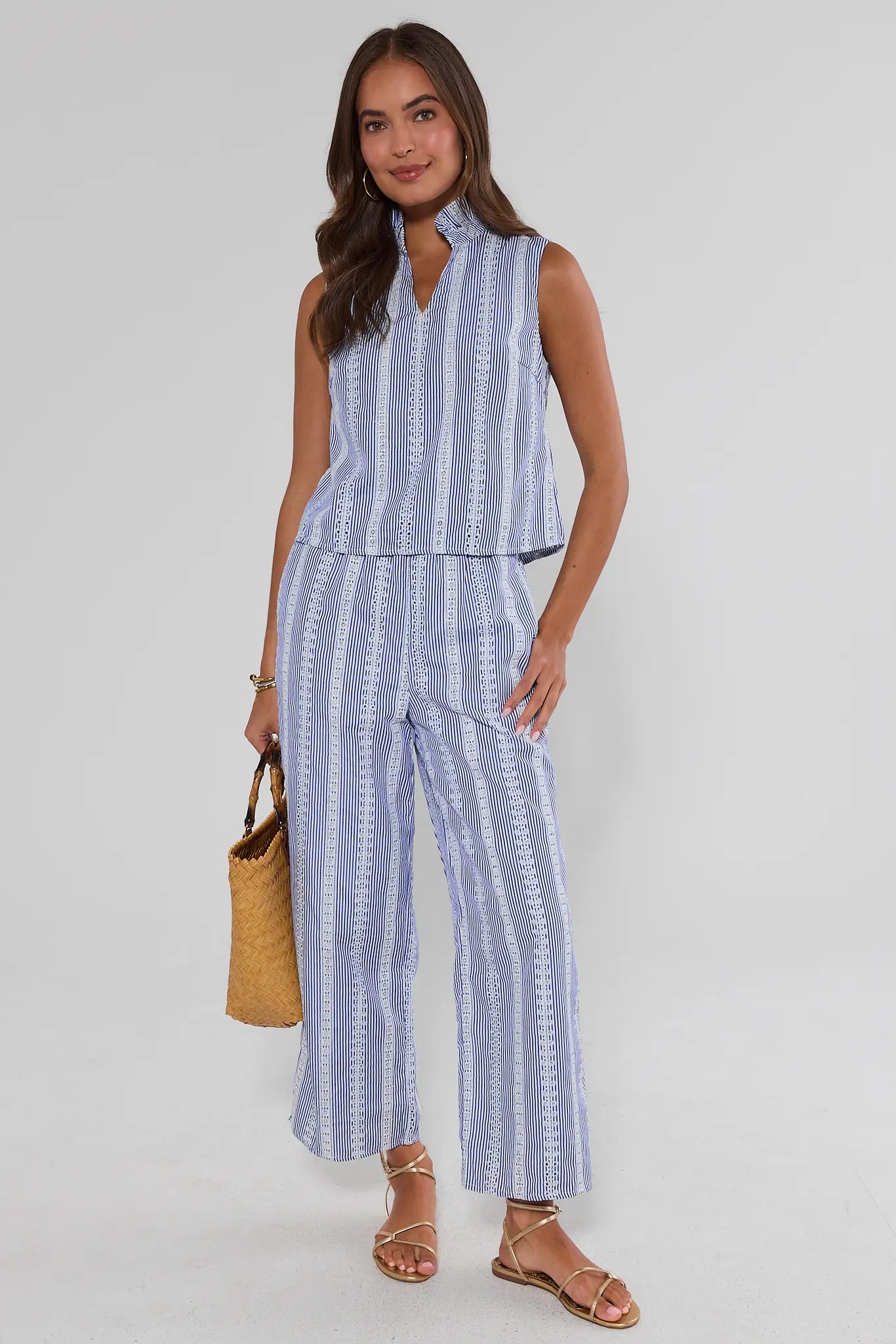 Woman wearing a blue and white striped outfit with a yellow bag on a plain background