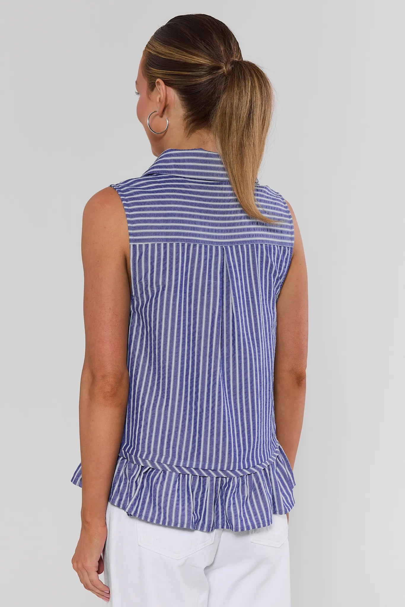 Woman standing wearing a blue and white striped sleeveless top against a plain background
