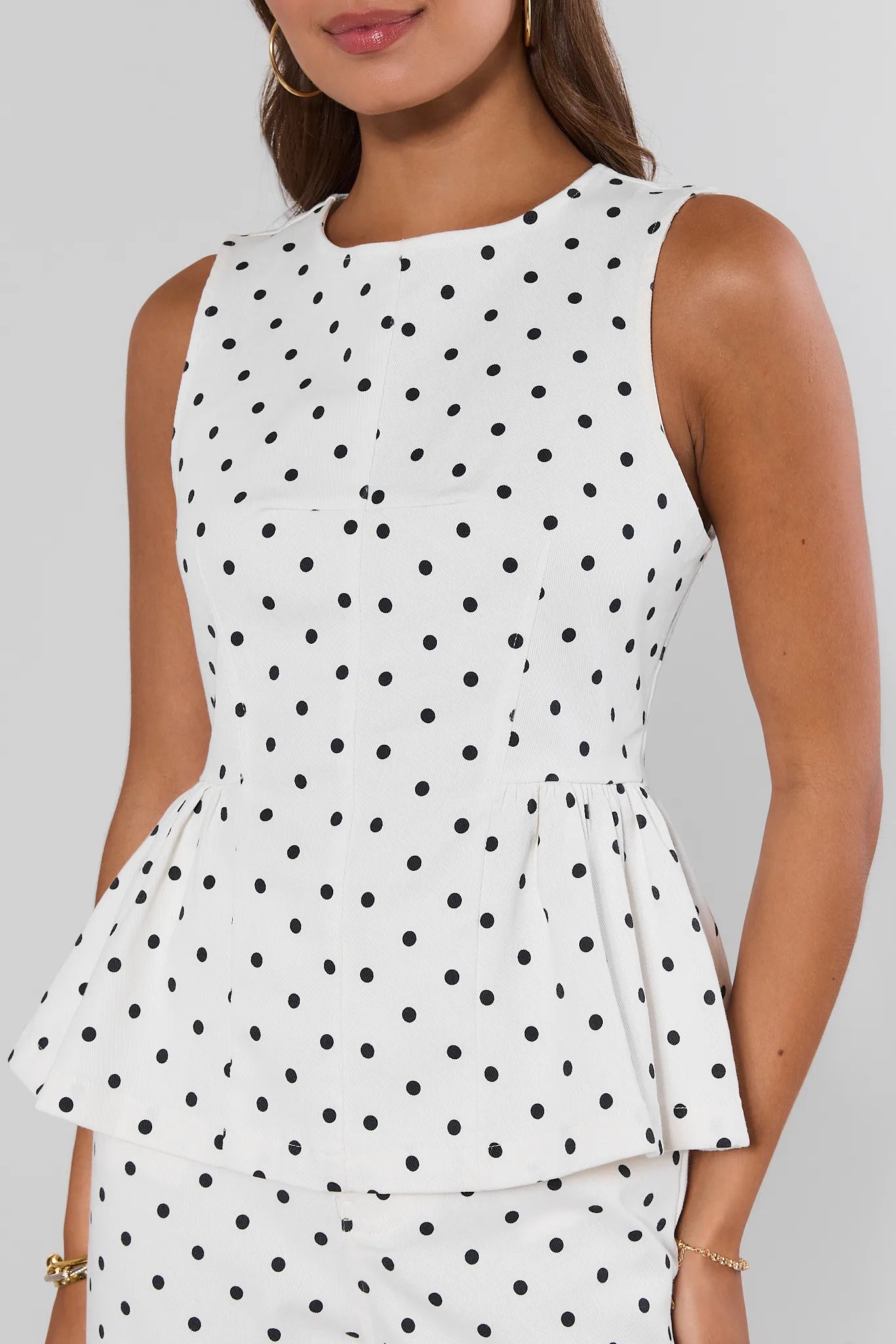 White sleeveless top with black polka dots worn by a person on a plain background close up