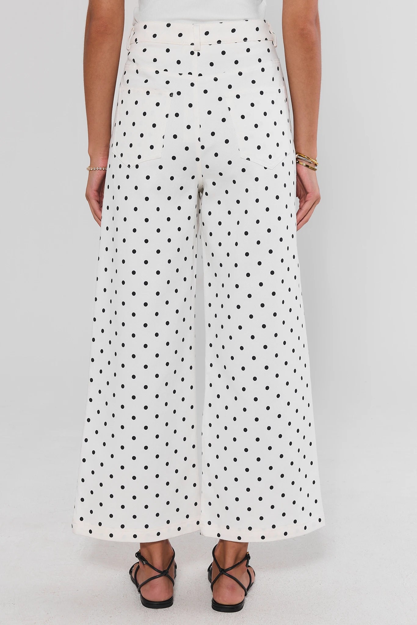 White pants with black polka dots worn by a person on a white background walking