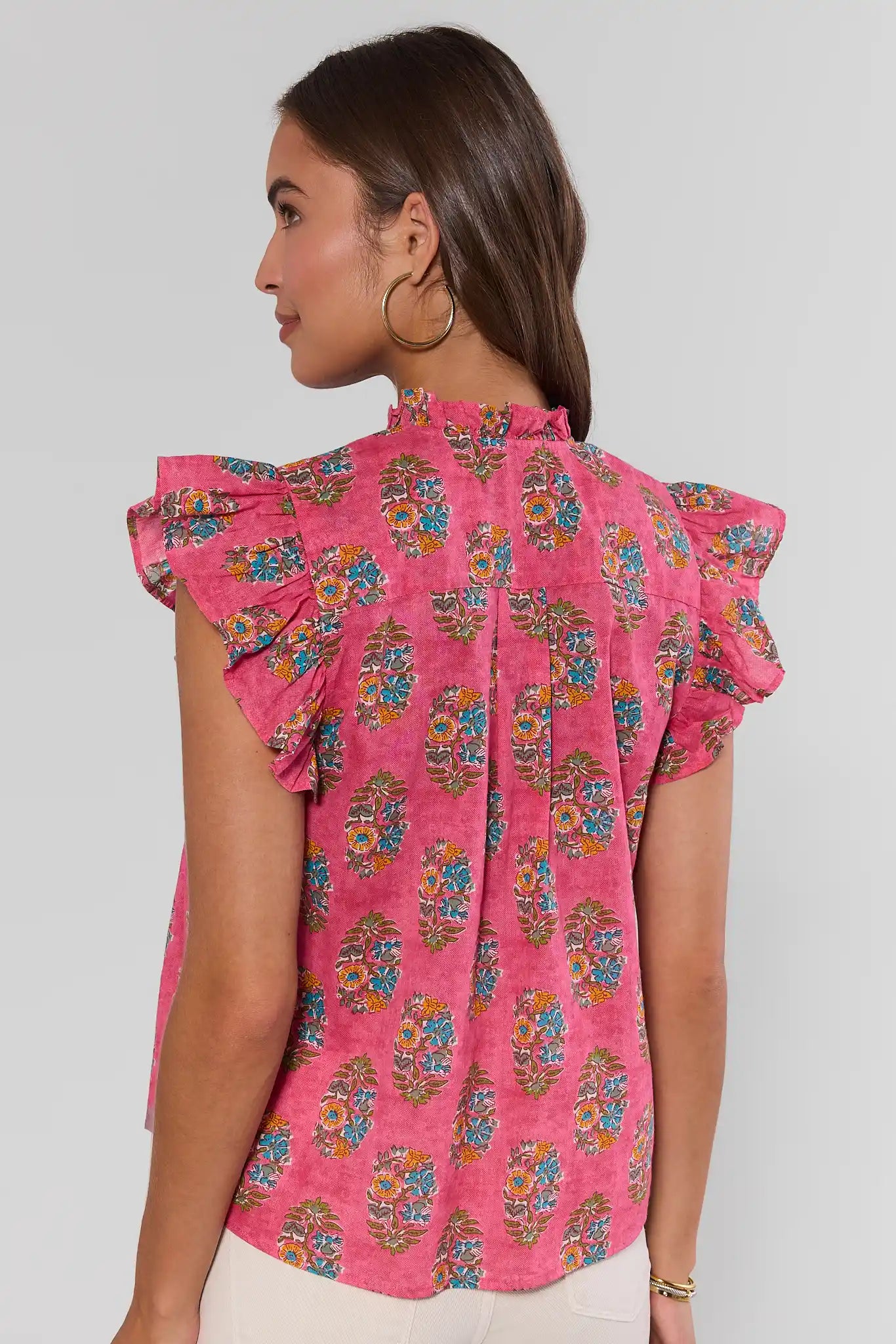 Woman wearing a pink floral blouse against a plain background turn