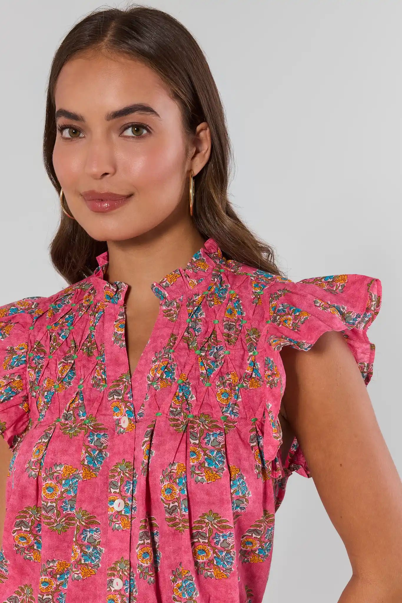 Woman wearing a pink floral dress against a plain background stand