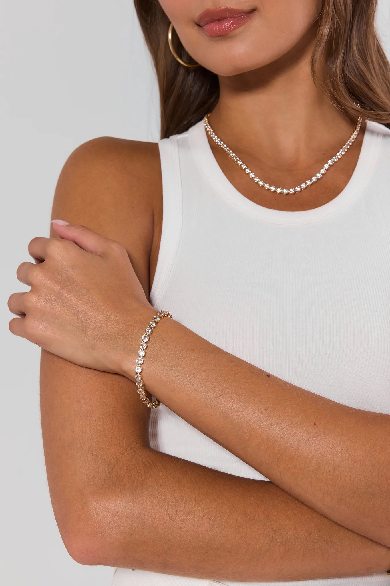 Woman wearing a tennis necklace and bracelet on a plain background