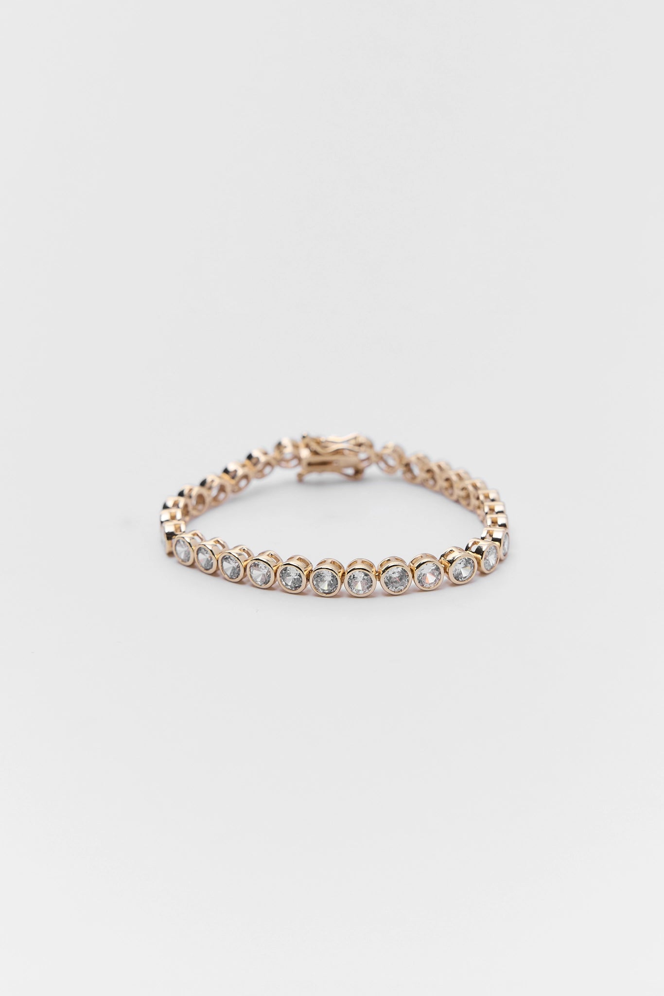 Gold bracelet with clear stones on a light gray background