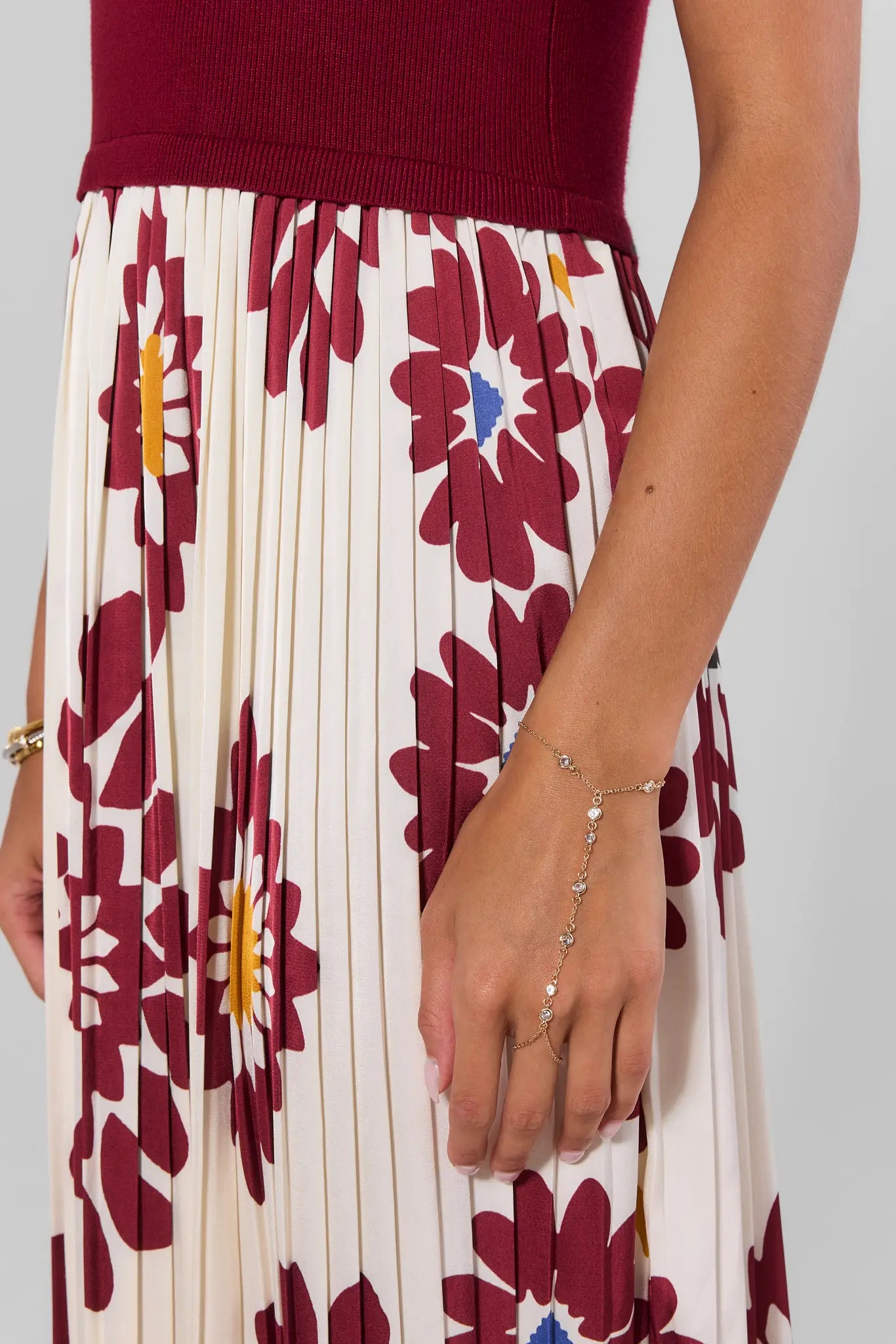 Woman wearing a gold hand chain bracelet and floral dress with a plain background