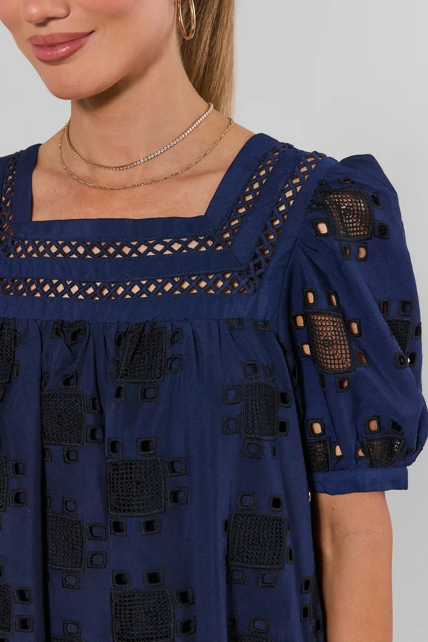 Navy blue dress with intricate cut-out patterns on a plain background close up