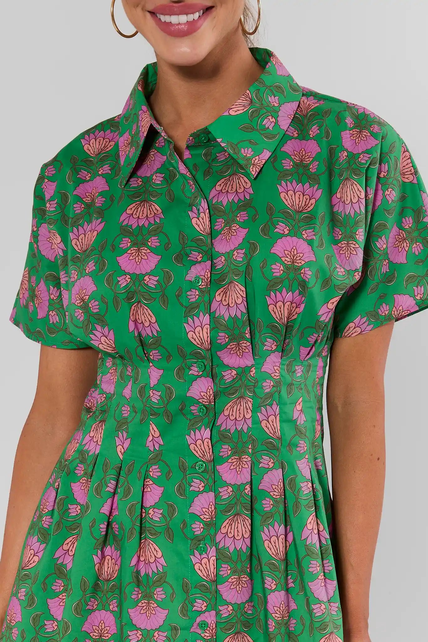 Woman wearing a green dress with pink floral pattern on a plain background close up