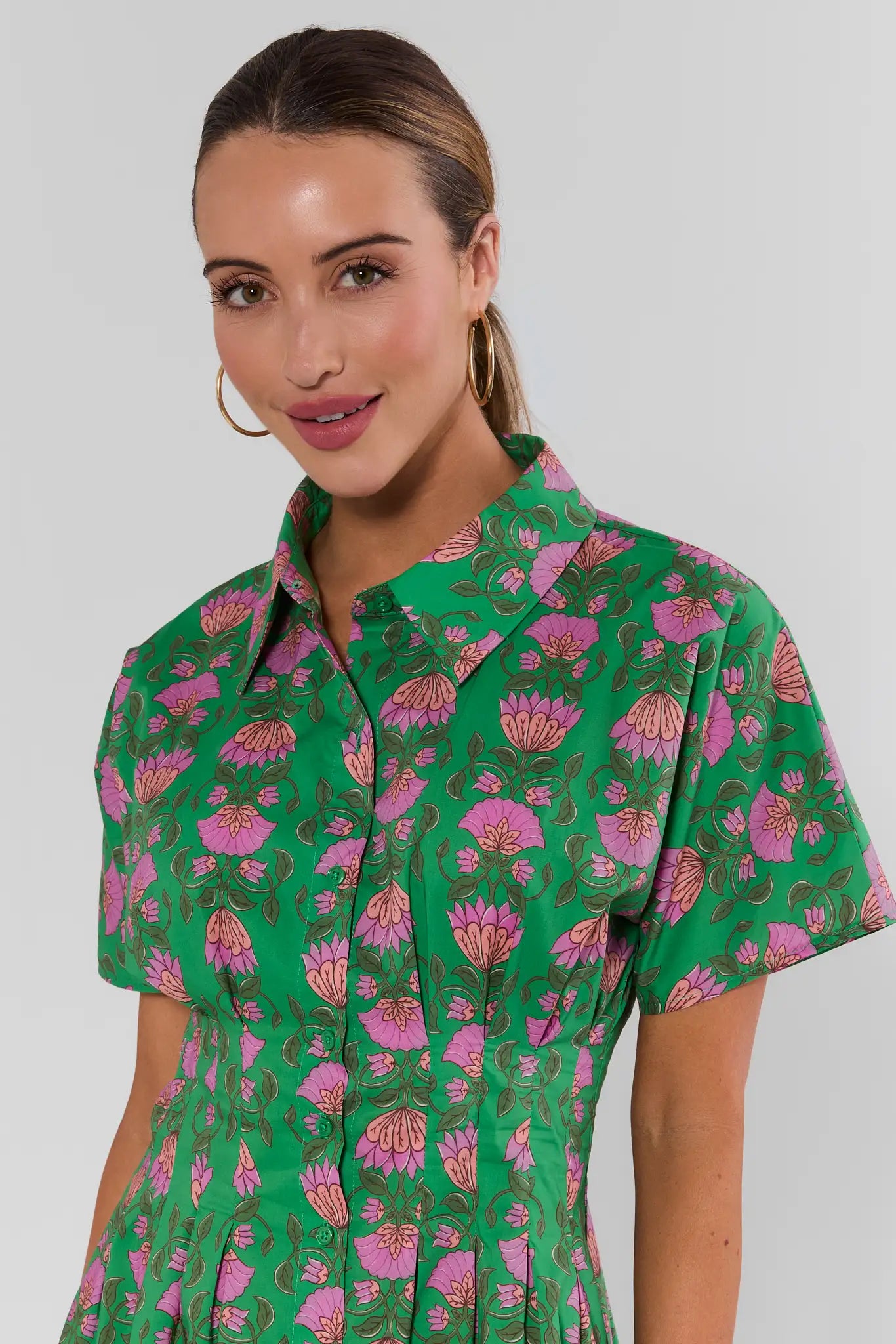 close up Woman wearing a green olivia dress with pink floral pattern against a white background
