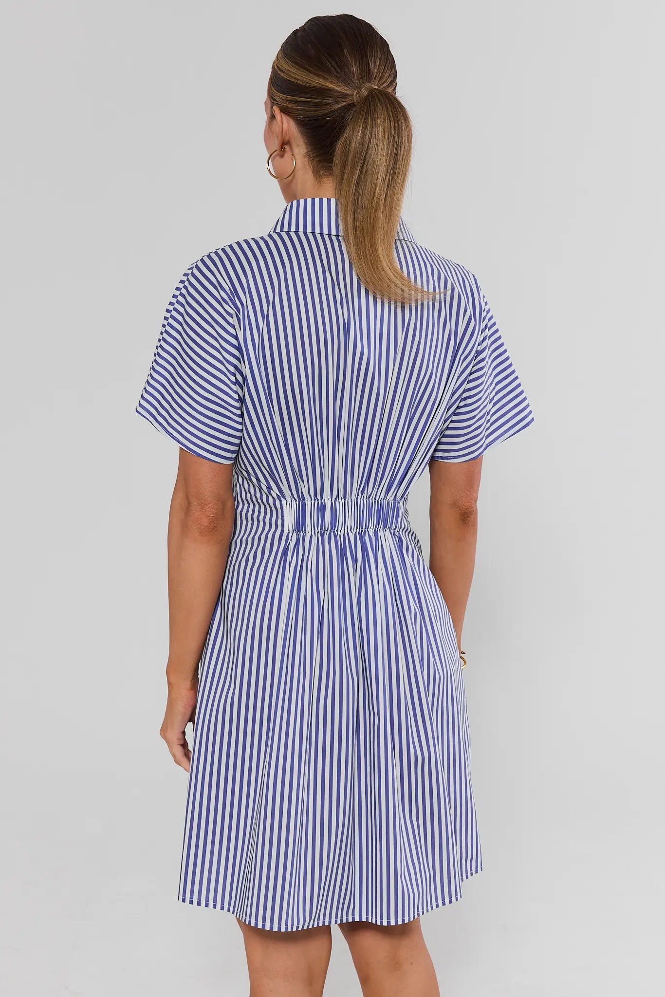 standing Woman wearing a blue and white striped dress on a plain background
