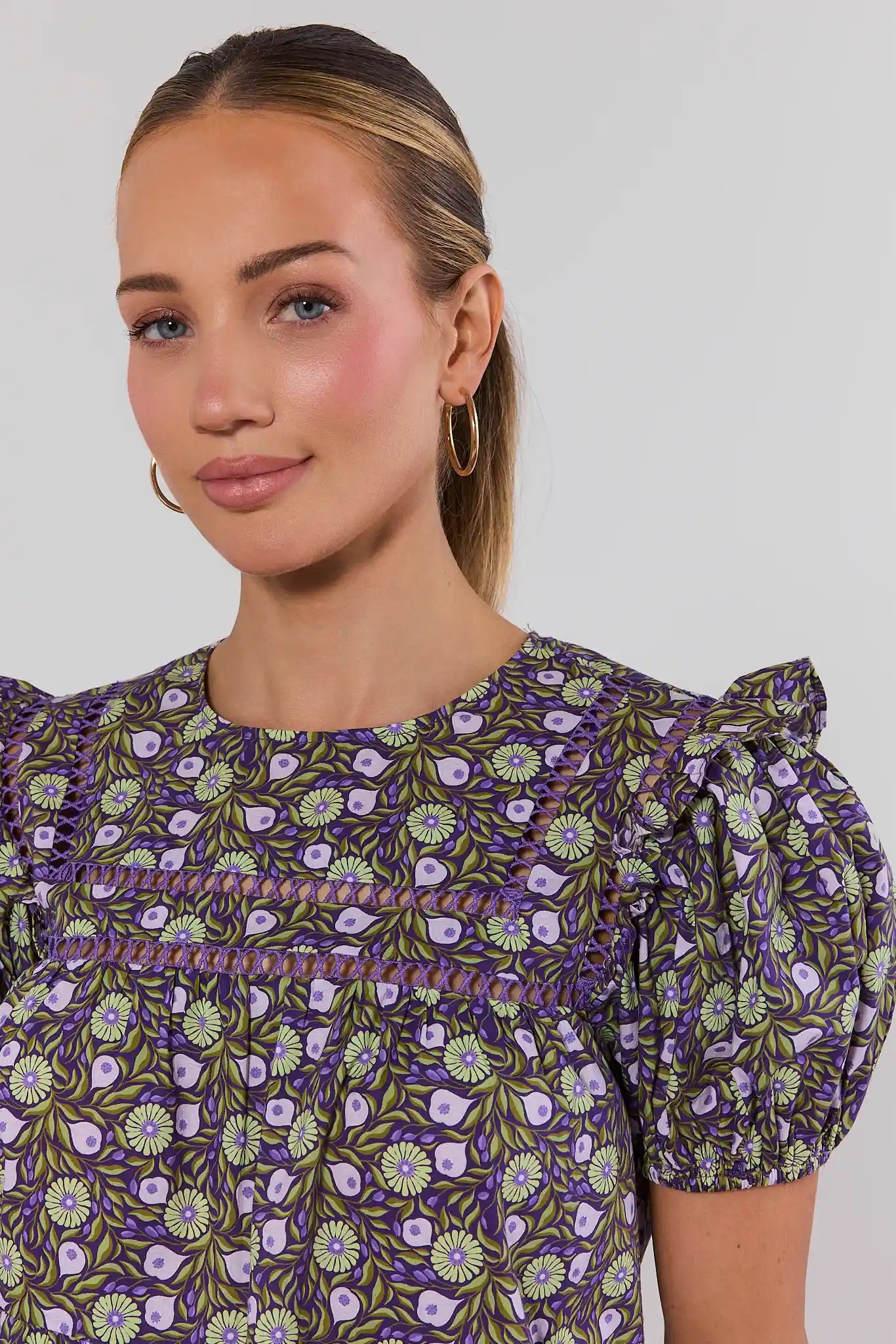 Woman wearing a purple floral dress against a plain background close up