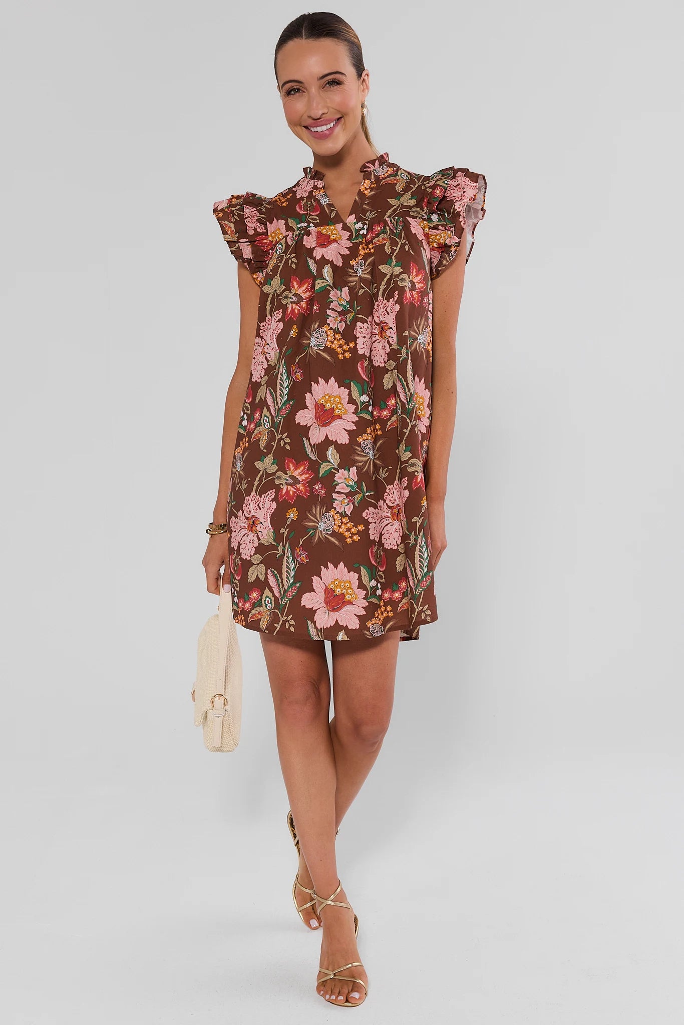 A woman modeling a brown short-sleeve floral dress with ruffled shoulders and a buttoned collar, on a white background.