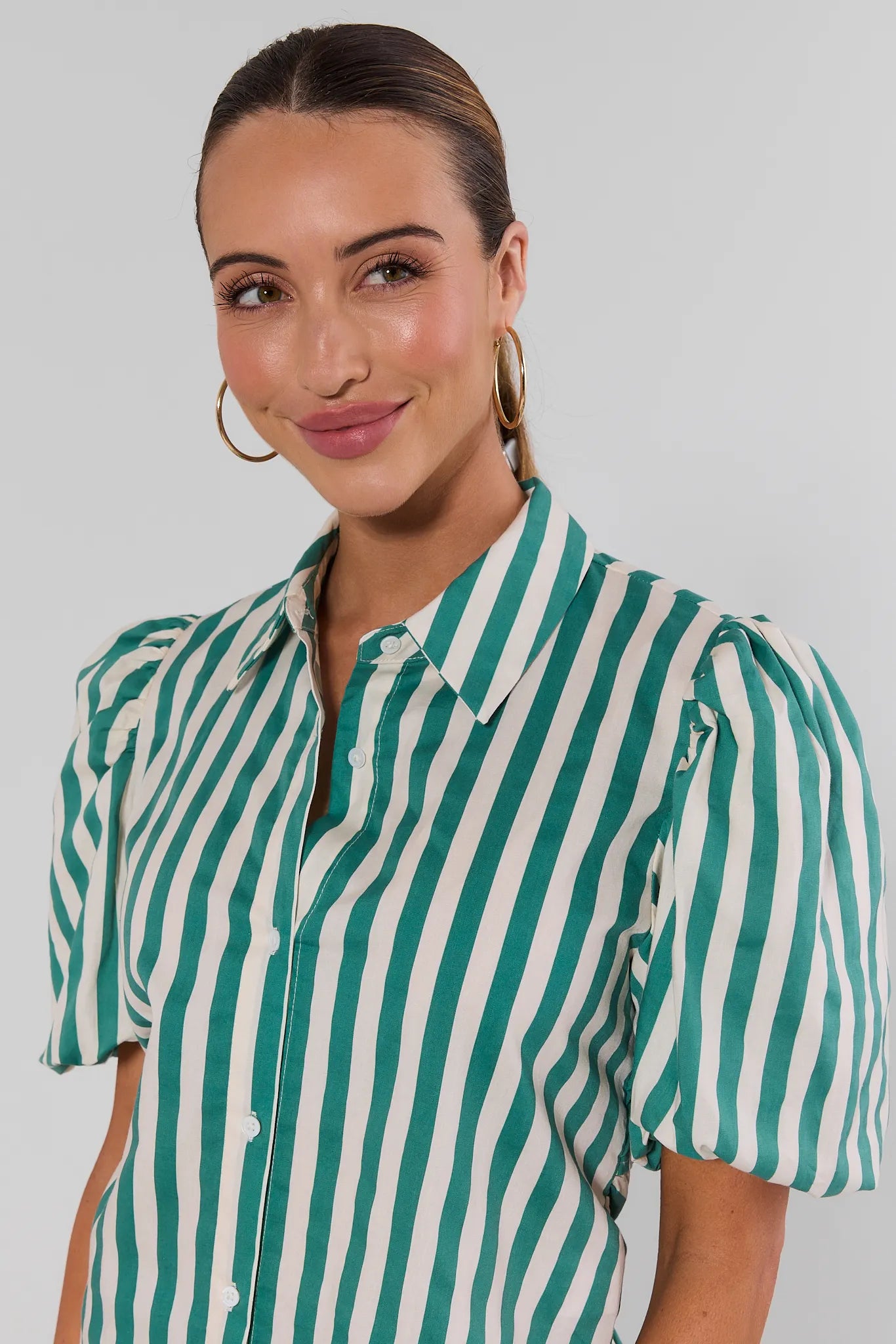close up A woman wearing a green and white vertically striped crop top with puff sleeves on a white background