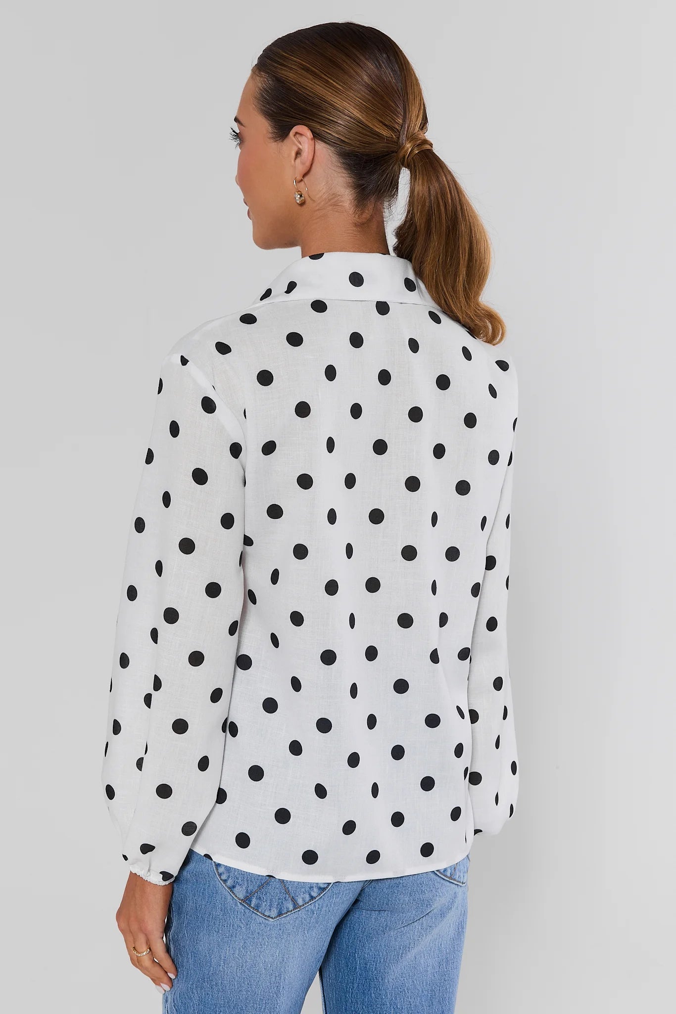 standing Woman wearing white polka dot top with jeans on a white background