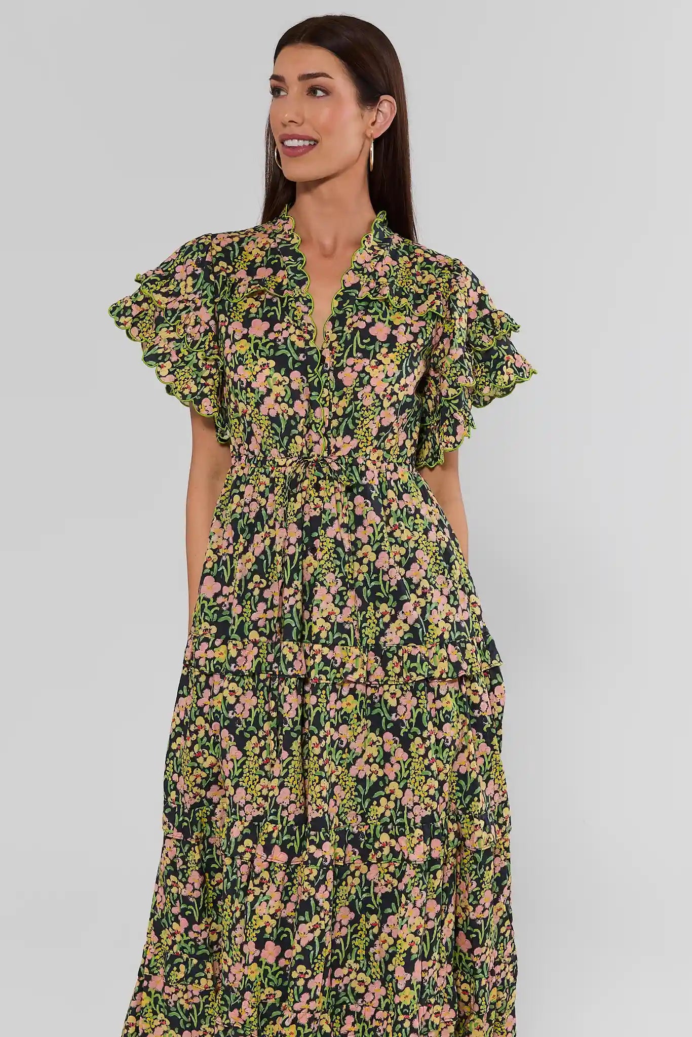 Woman standing wearing a long-sleeved, V-neck maxi dress with a green, yellow, and pink floral print, against a plain light background.