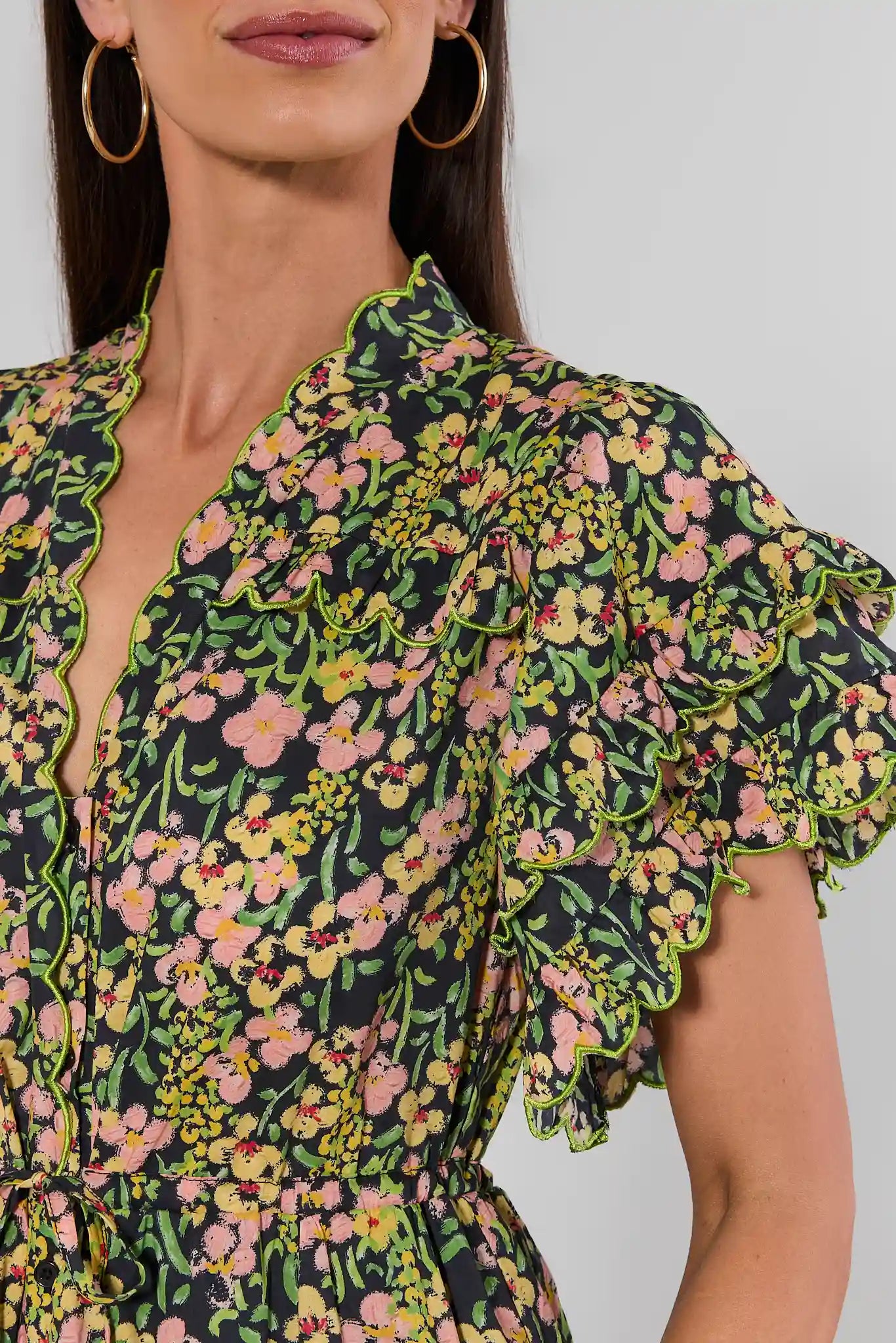 close up woman standing wearing a long-sleeved, V-neck maxi dress with a green, yellow, and pink floral print, against a plain light background.