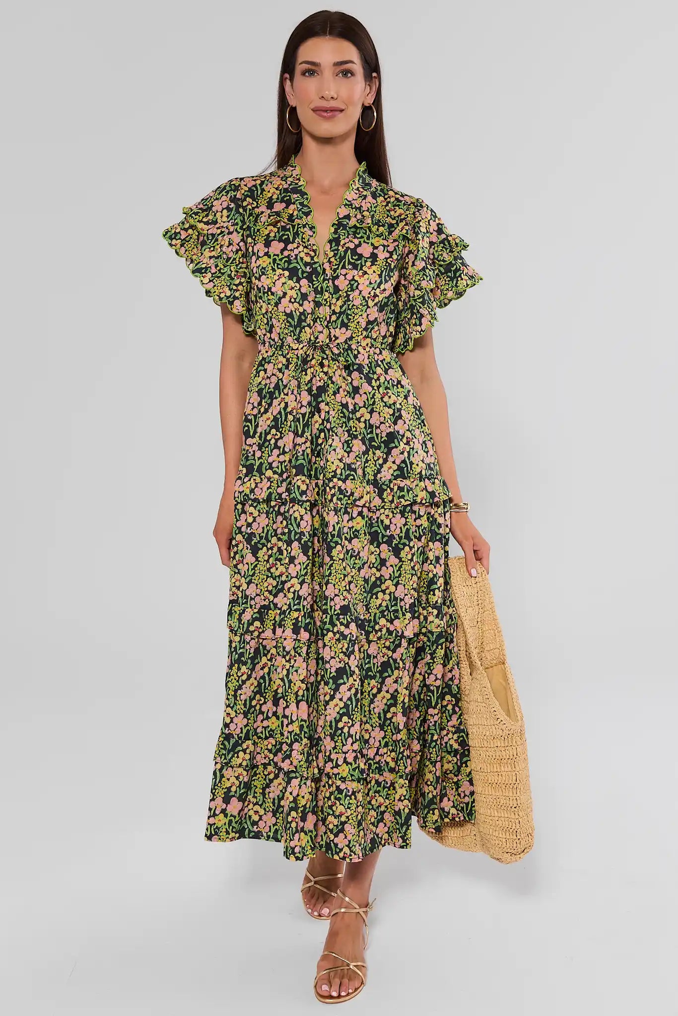 Woman walking wearing a long-sleeved, V-neck maxi dress with a green, yellow, and pink floral print, against a plain light background.