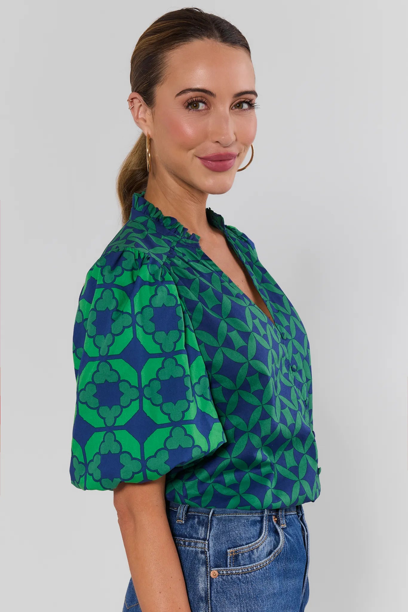 A woman wearing a green and blue patterned short-sleeve blouse with puff sleeves against a white background