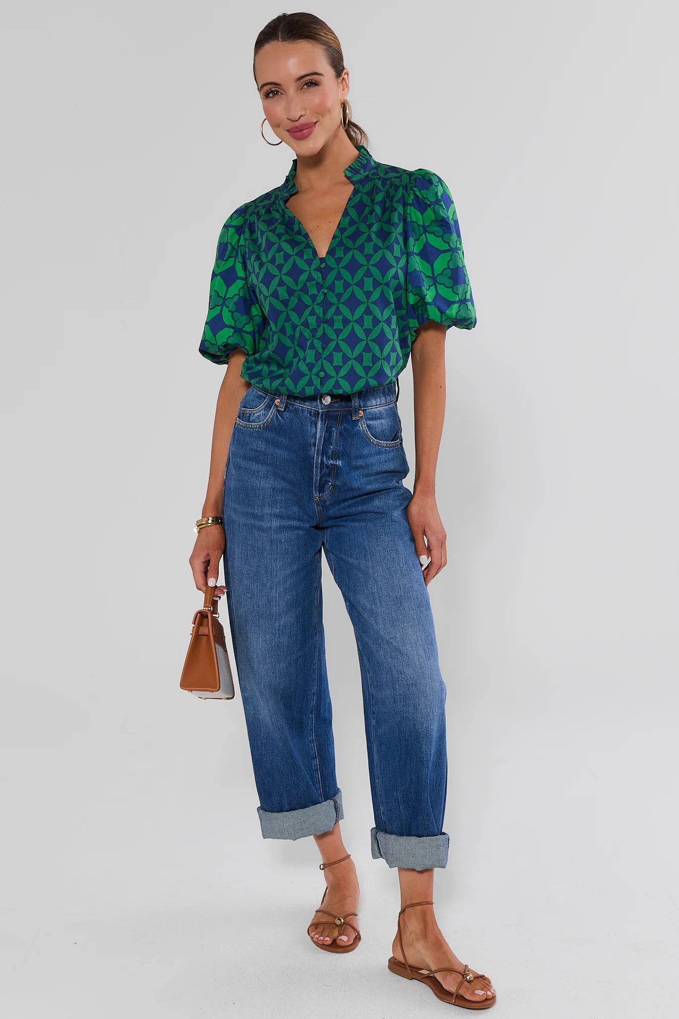 A woman wearing a green and blue patterned short-sleeve blouse with puff sleeves and jeans against a white background