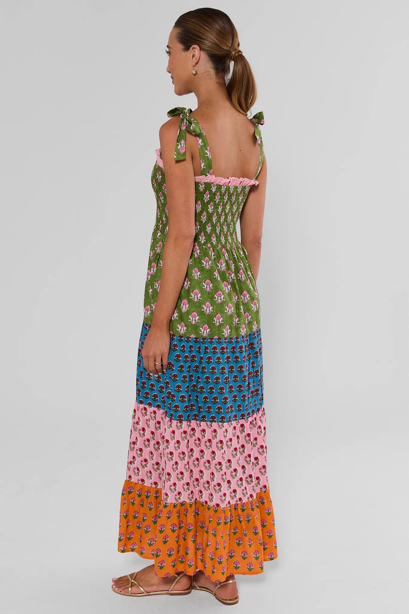 A woman modeling a sleeveless tiered maxi dress with a colorful patchwork print,  on a white background
