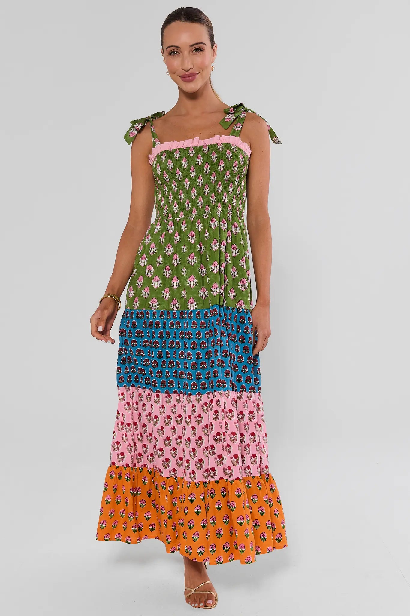 A woman walking modeling a sleeveless tiered maxi dress with a colorful patchwork print, 