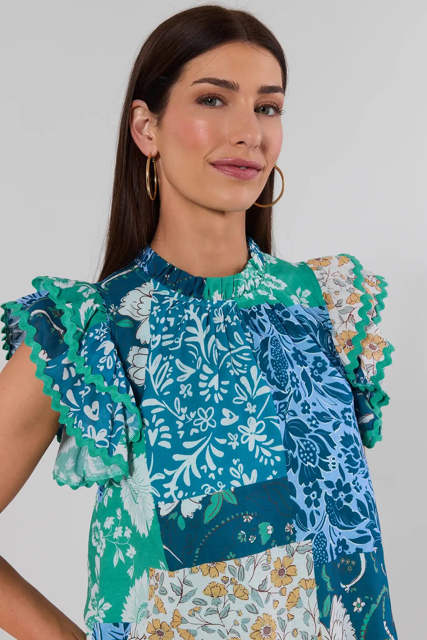close up A woman with brown hair wearing a colorful patchwork floral blouse with ruffled sleeves, with a white background