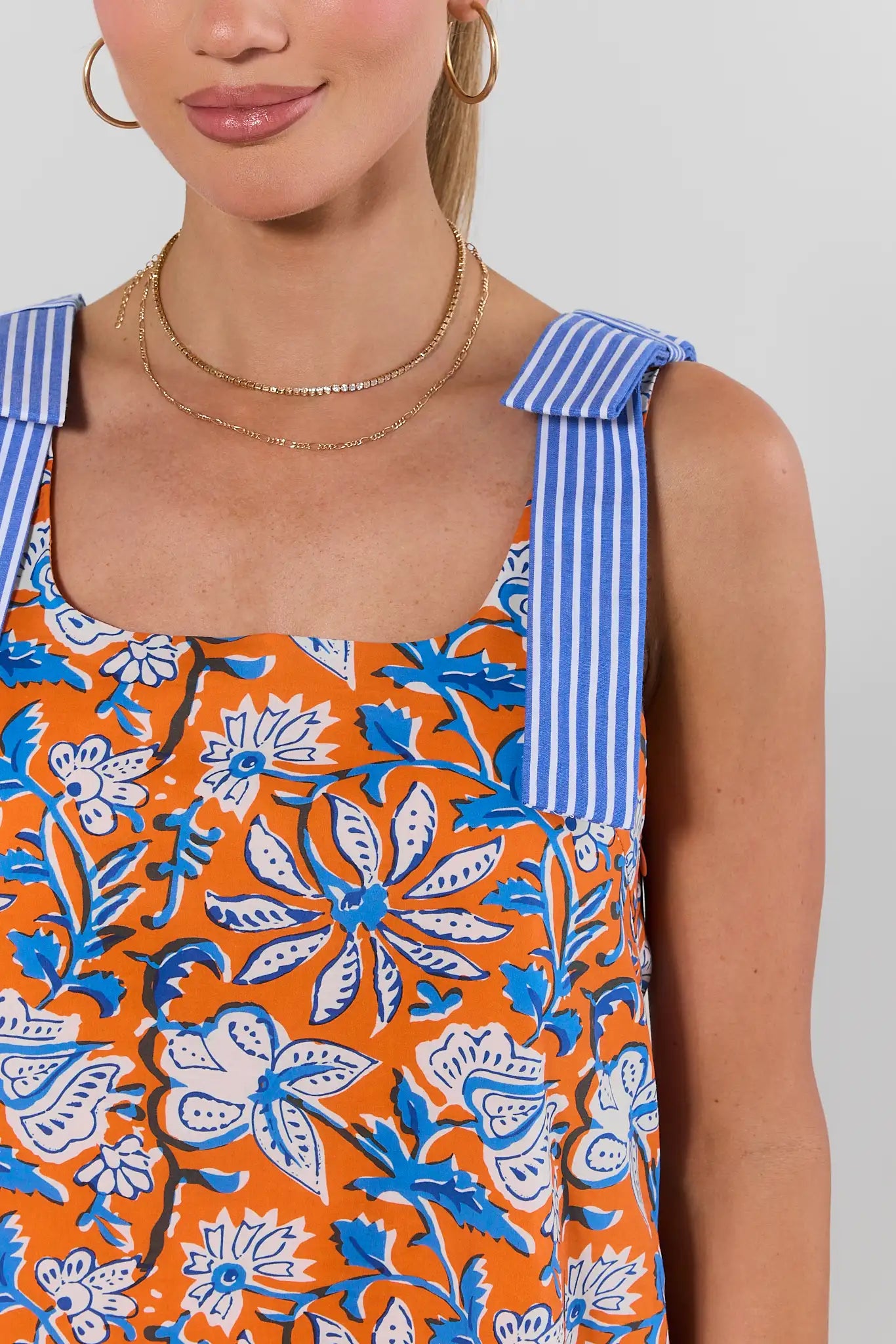close up Woman wearing Orange Floral Print Shift Dress with blue striped bows on straps on a white background