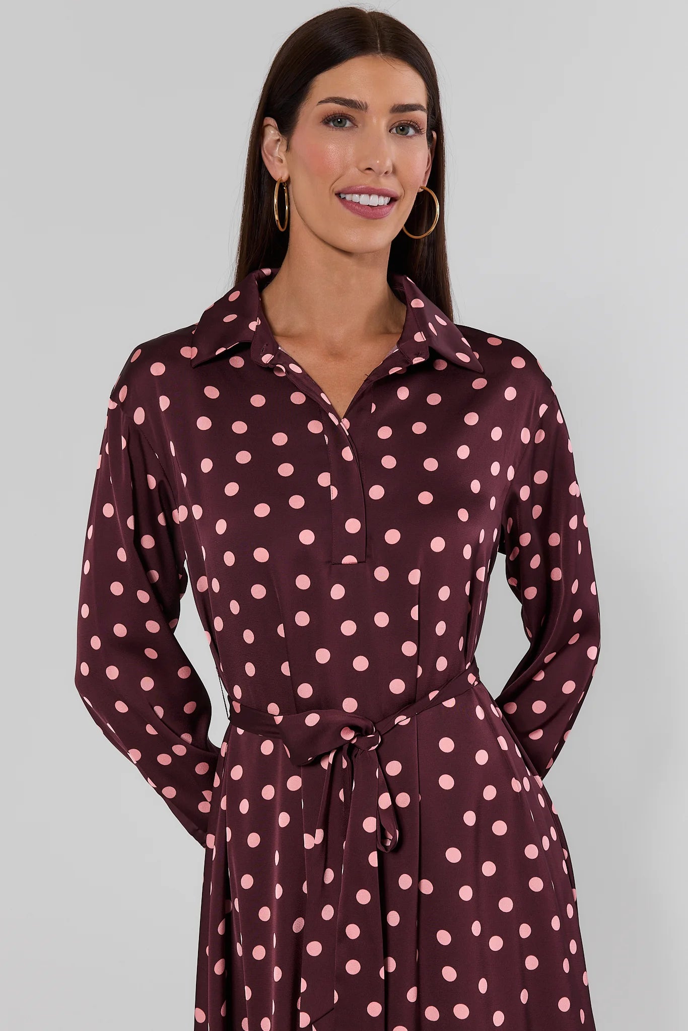 woman standing wearing brown polka dot dress on white background 