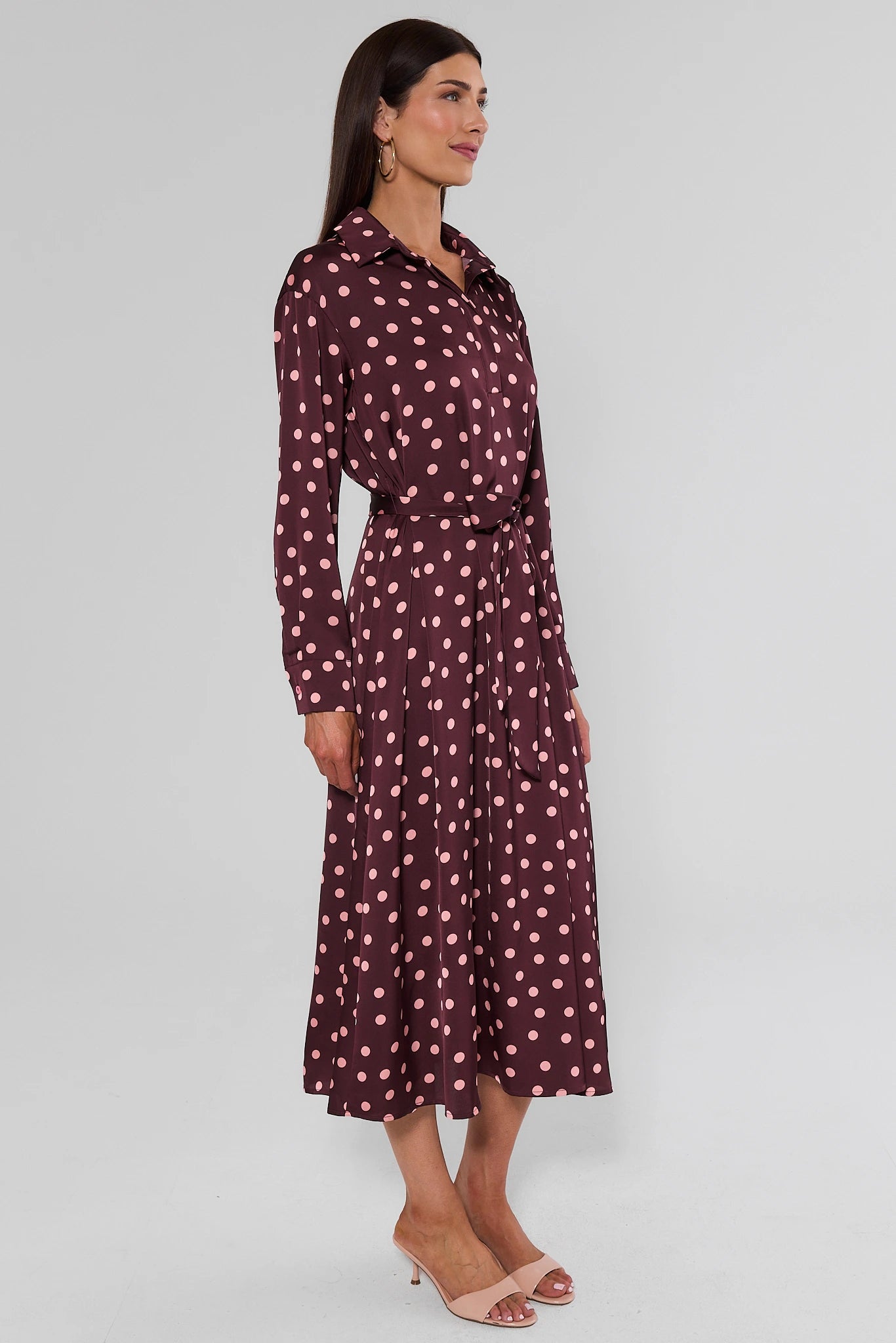 woman standing wearing brown polka dot dress on white background side
