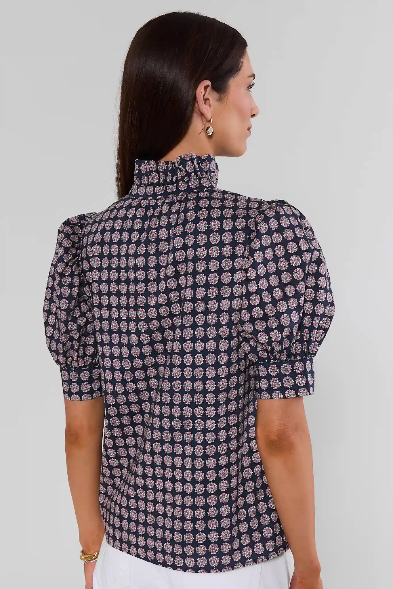 Woman turned wearing a geometric navy and purple top with white jeans on a cream background